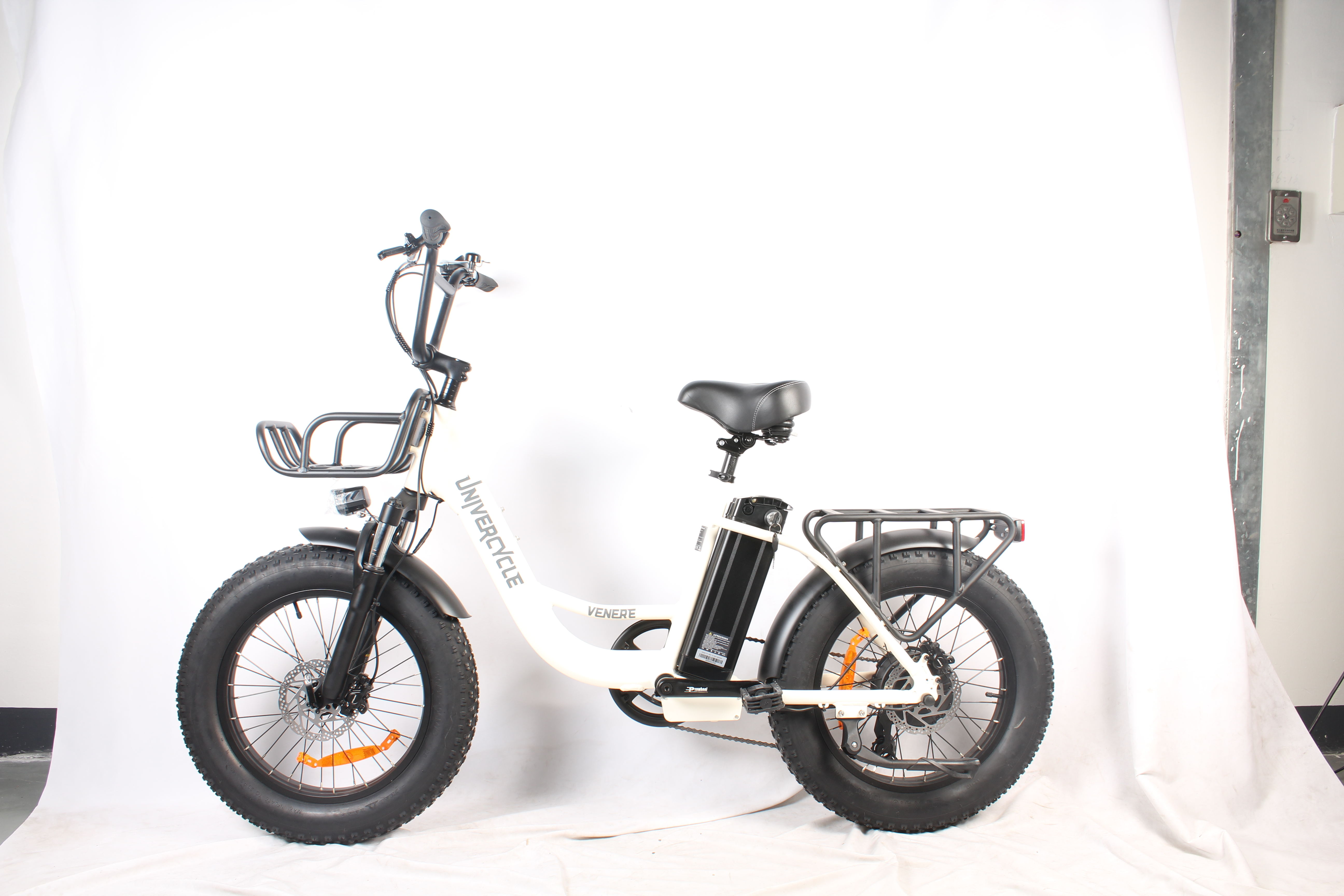 Una bicicletta elettrica bianco sporco, pneumatici, sella e manubrio neri. Ha un cestino, un portapacchi e una batteria.