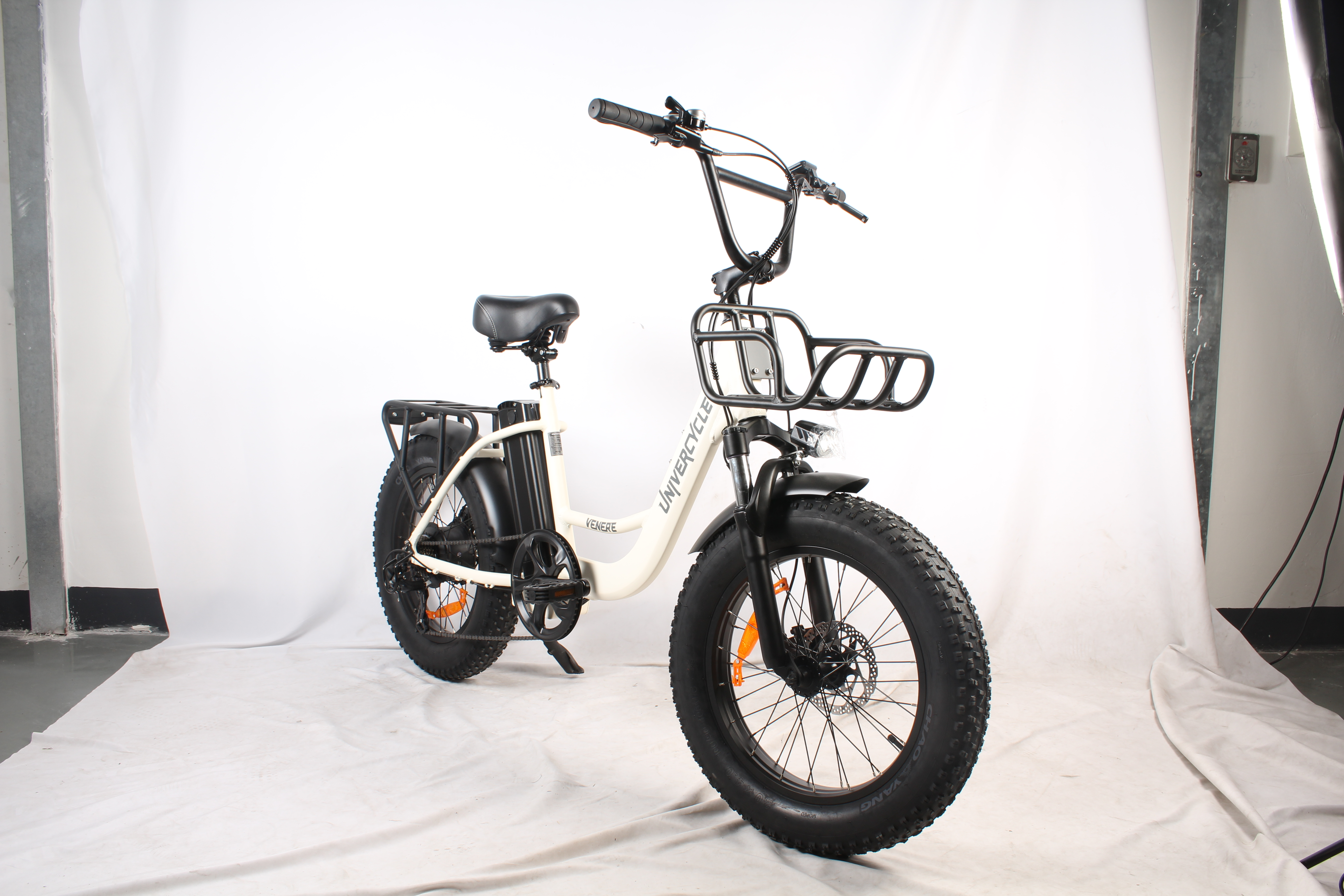 Bicicletta elettrica bianca e nera con pneumatici larghi, cestino e sedile. Lo sfondo è bianco.