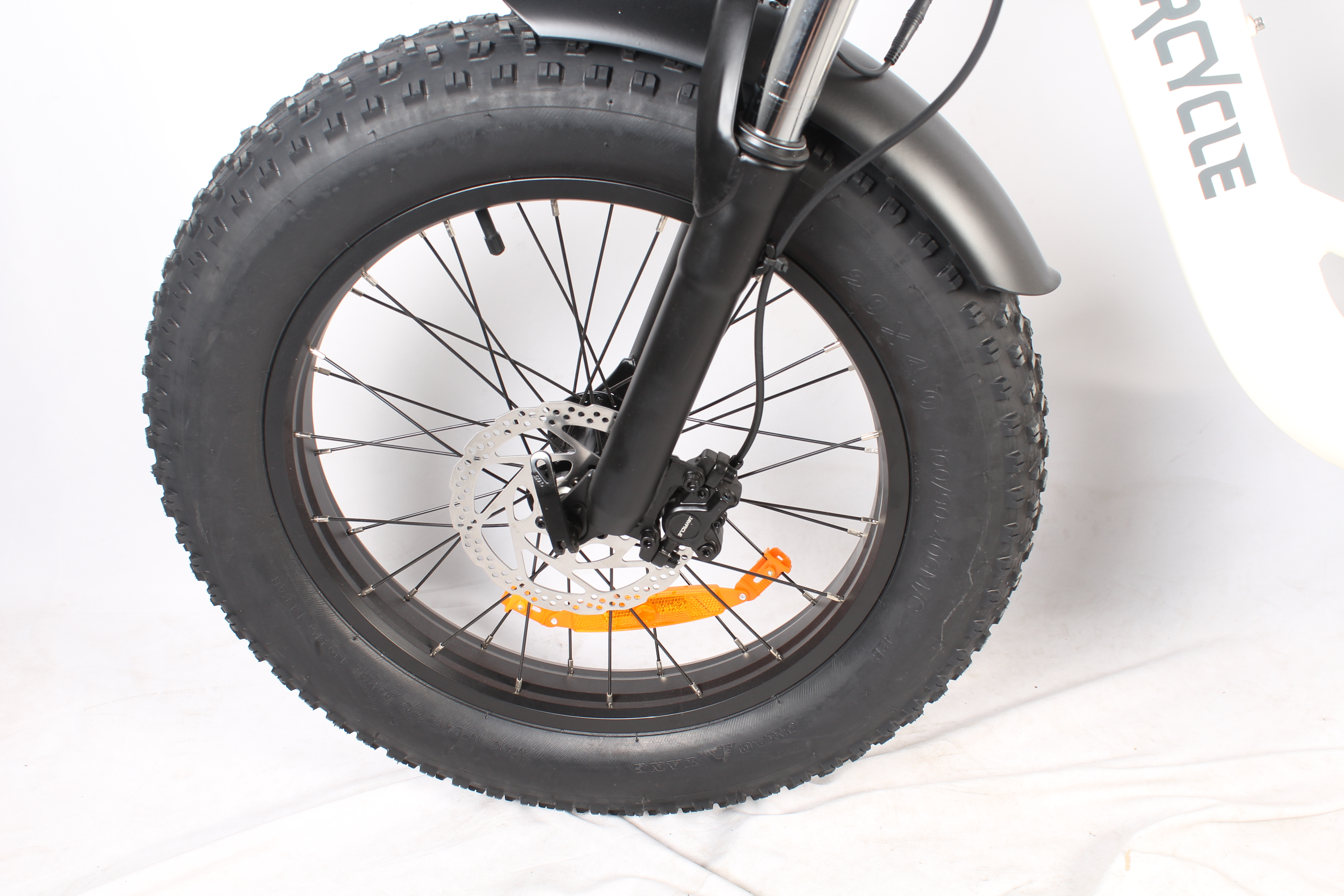 Una ruota di e-bike nera con uno pneumatico spesso. È visibile un freno a disco argentato. Sfondo bianco.