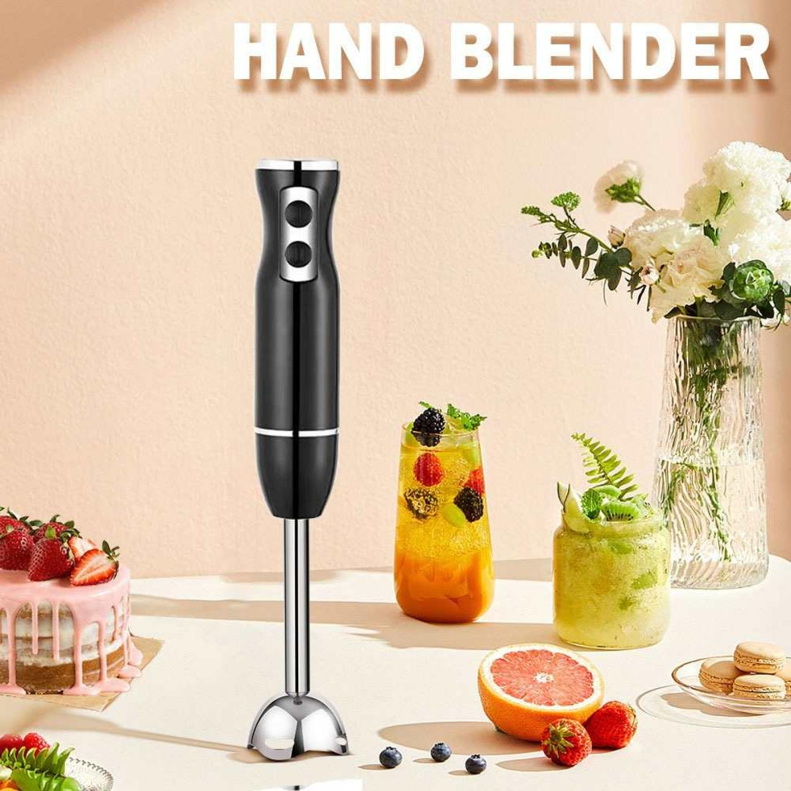 Ein Stabmixer mit verschiedenen Früchten, Smoothies, Kuchen und Macarons auf einem Tisch. Weiße Blumen in einer Vase.