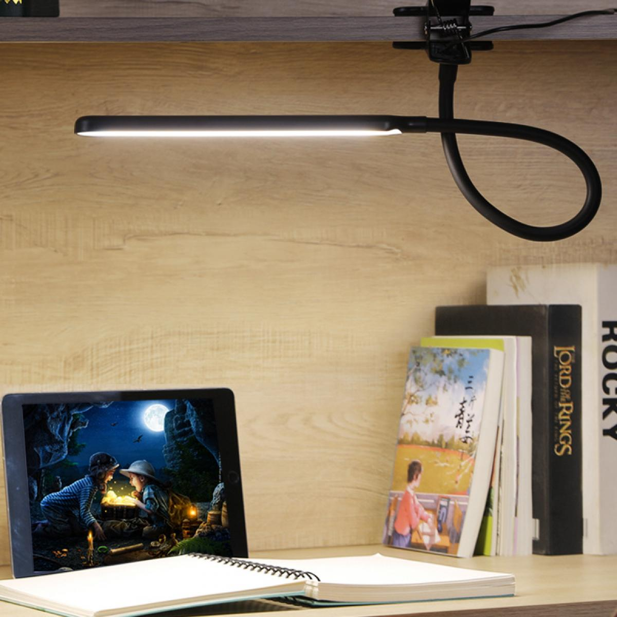 Eine Schreibtischlampe beleuchtet ein Tablet, das eine Fantasieszene zeigt. Bücher, ein Notizblock und ein Holzuntergrund vervollständigen das Setup.