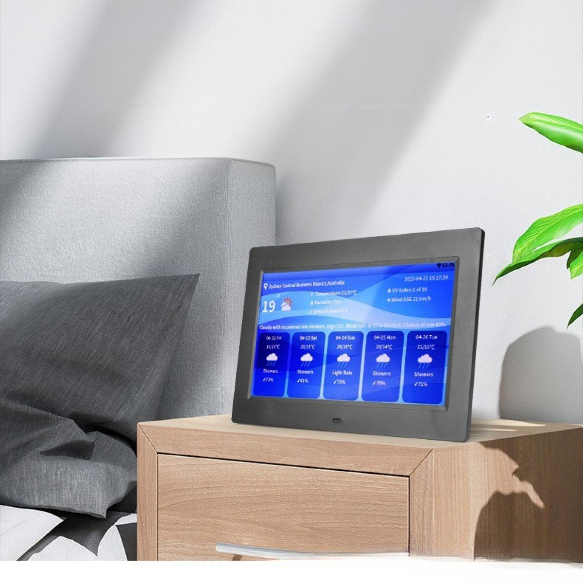 Eine digitale Wetterstation zeigt die Wettervorhersage für Sydney. Sie steht auf einem Nachttisch aus Holz neben einem Bett mit einem grauen Kissen.