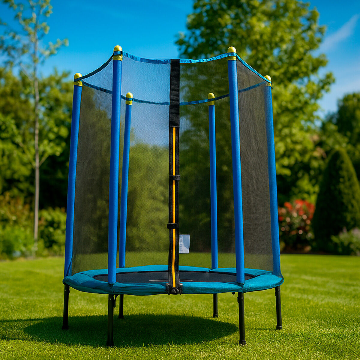 Un trampolín azul con red de seguridad sobre césped verde. Postes azules sostienen la red. Árboles y cielo en el fondo.