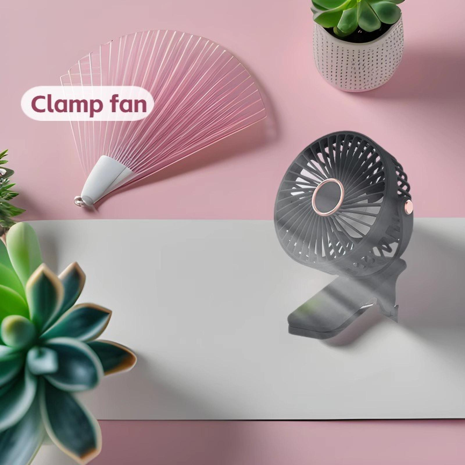 Ein kleiner grauer Klemmventilator, ein pinkfarbener Ventilator und eine Sukkulente befinden sich auf einer rosa und weißen Oberfläche.