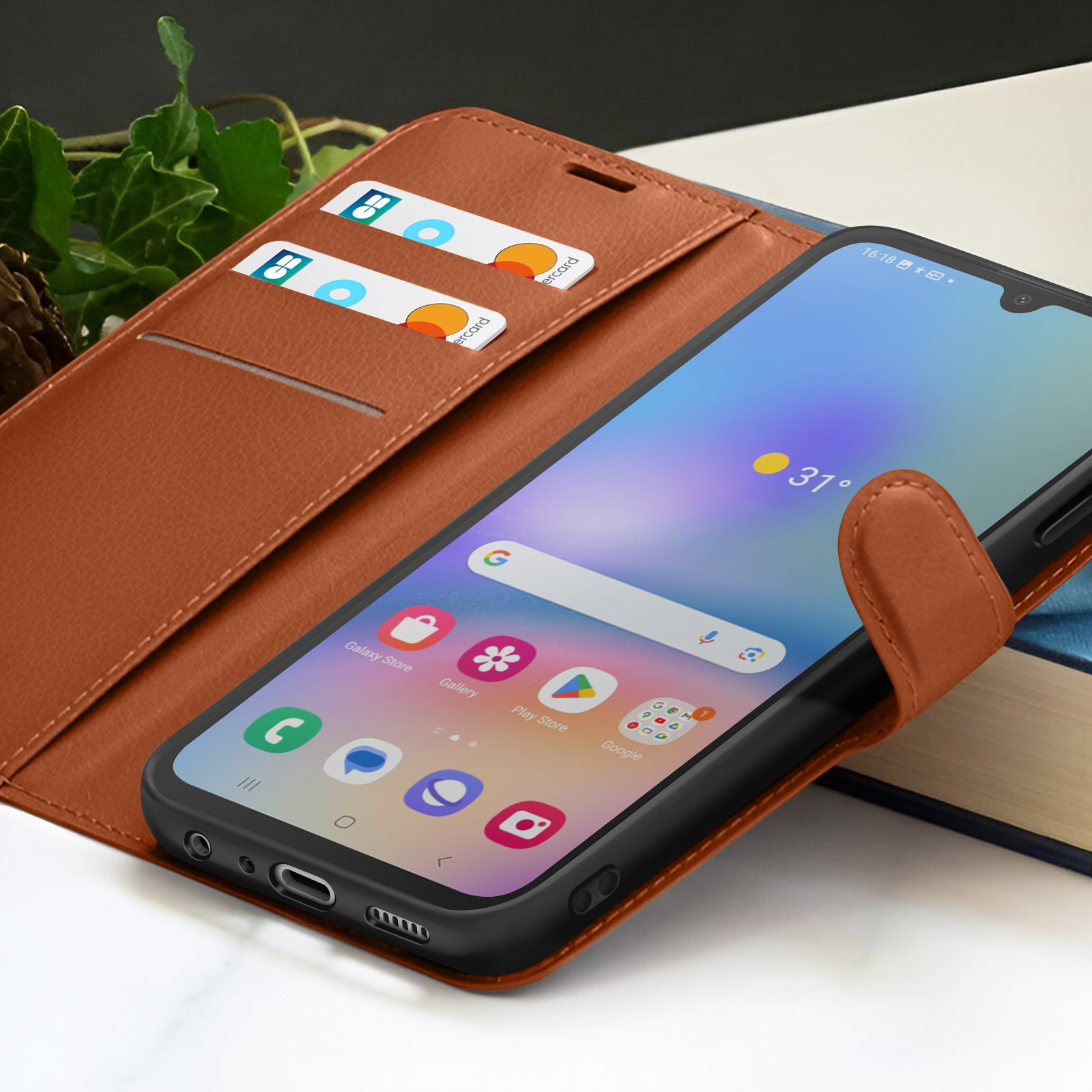 Un smartphone dans un étui en cuir marron affiche l'écran d'accueil. Des cartes de crédit sont dans l'étui. La température est de 31 degrés.