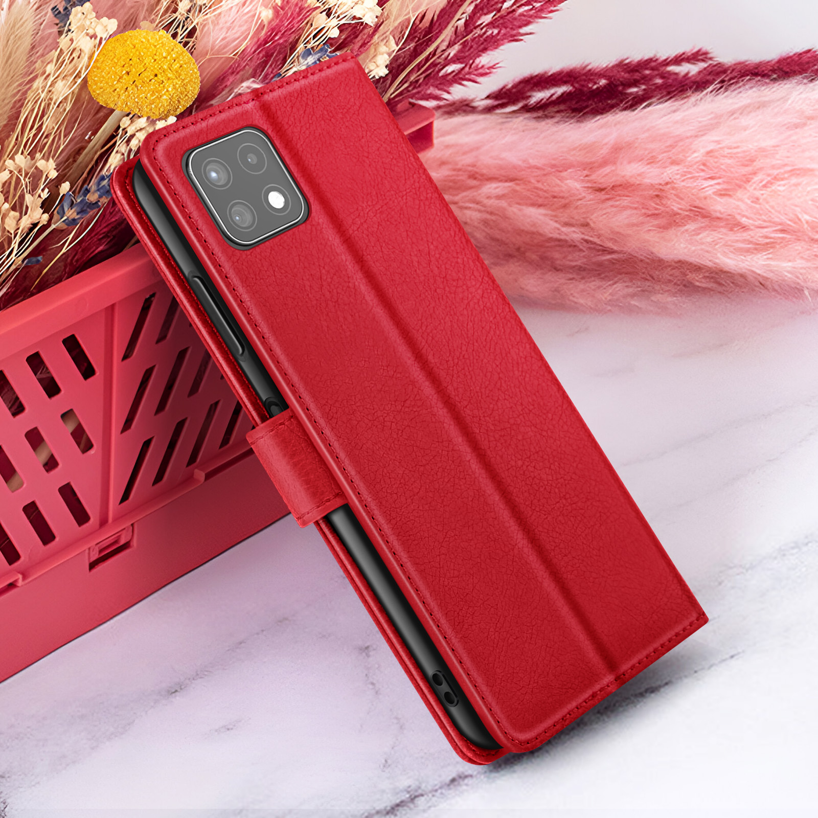 Rode telefoonhoes met een telefoon erin, rustend tegen een rode mand en roze bloemen.
