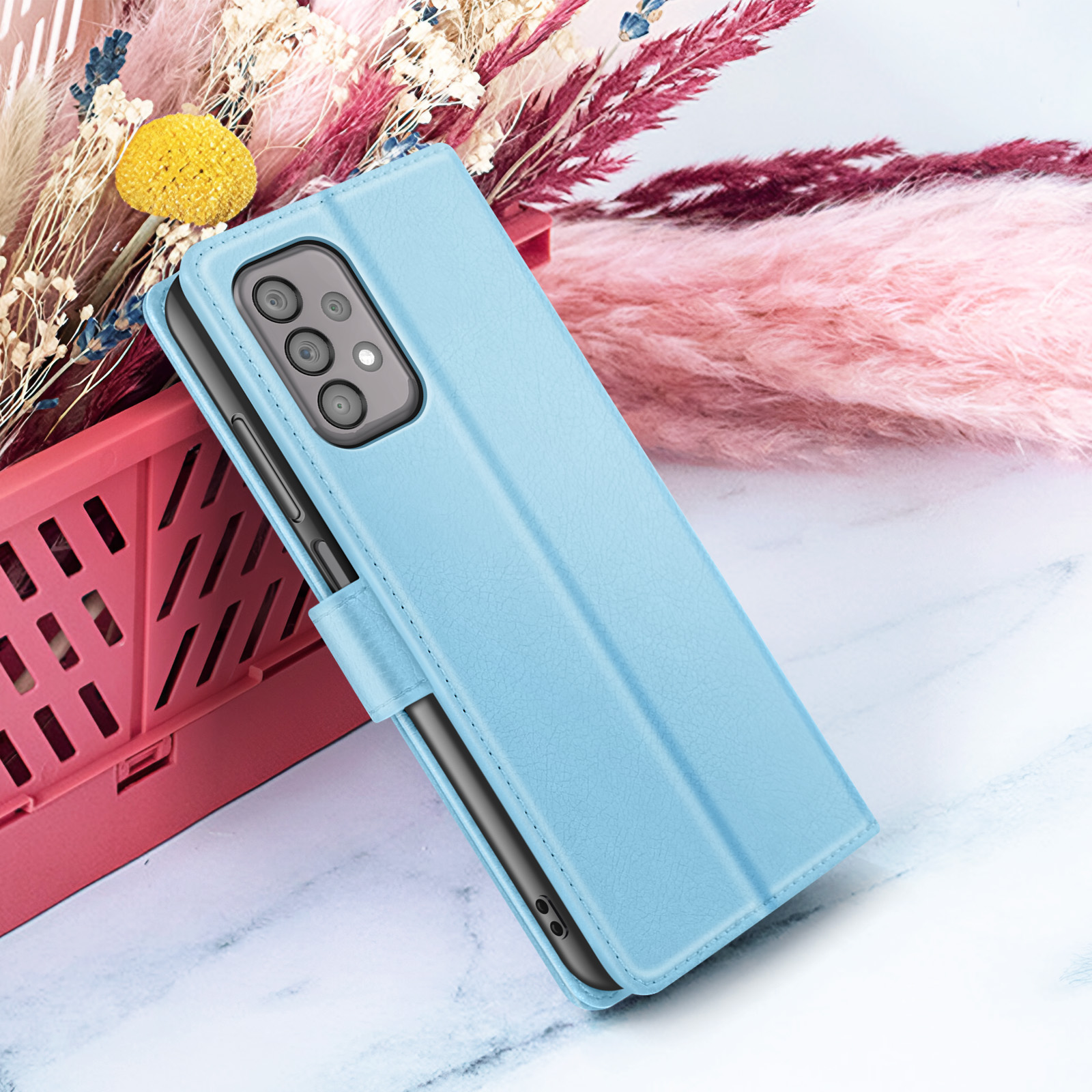 Eine hellblaue Handyhülle ist geöffnet und zeigt ein Telefon. Im Hintergrund sind Blumen. Die Hülle liegt auf einer Marmoroberfläche.