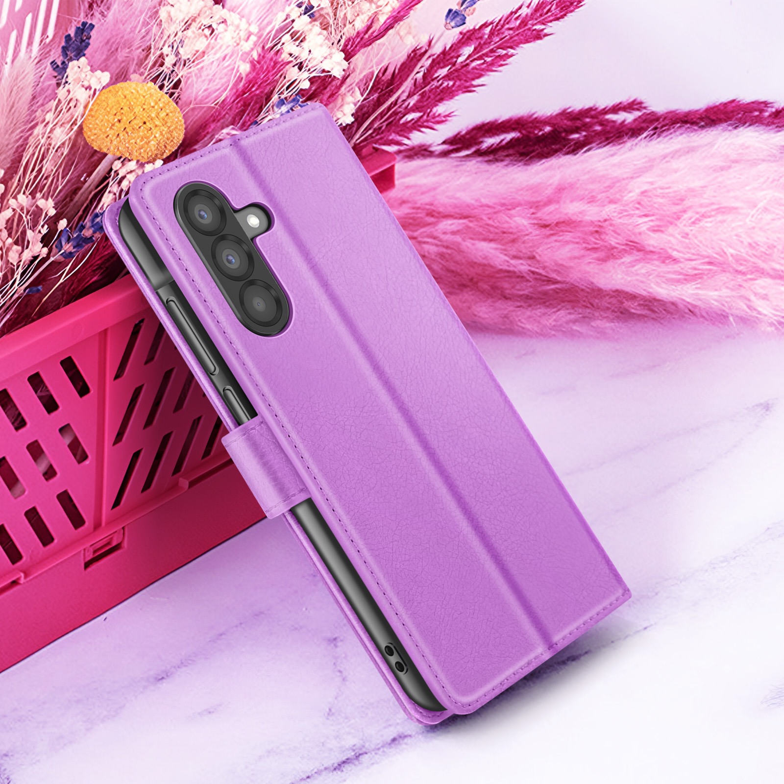 Een paarse telefoonhoes met drievoudige camera staat op een wit marmeren oppervlak met roze bloemenachtergrond.