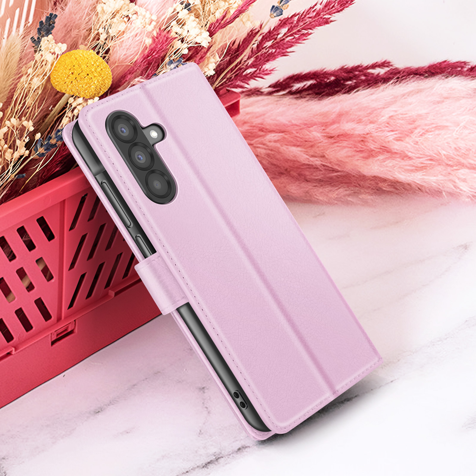 Een roze telefoonhoesje, met een uitsparing voor de camera, voor bloemen en een marmeren achtergrond.