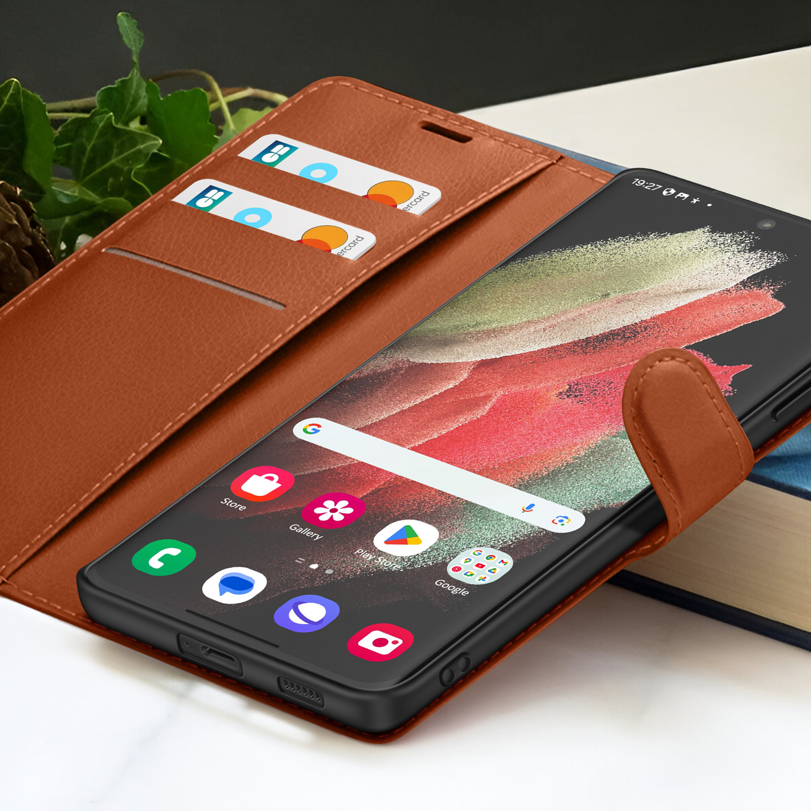 Un smartphone dans un étui en cuir marron, ouvert pour afficher l'écran. Des cartes de crédit sont visibles dans l'étui. Livres en arrière-plan.