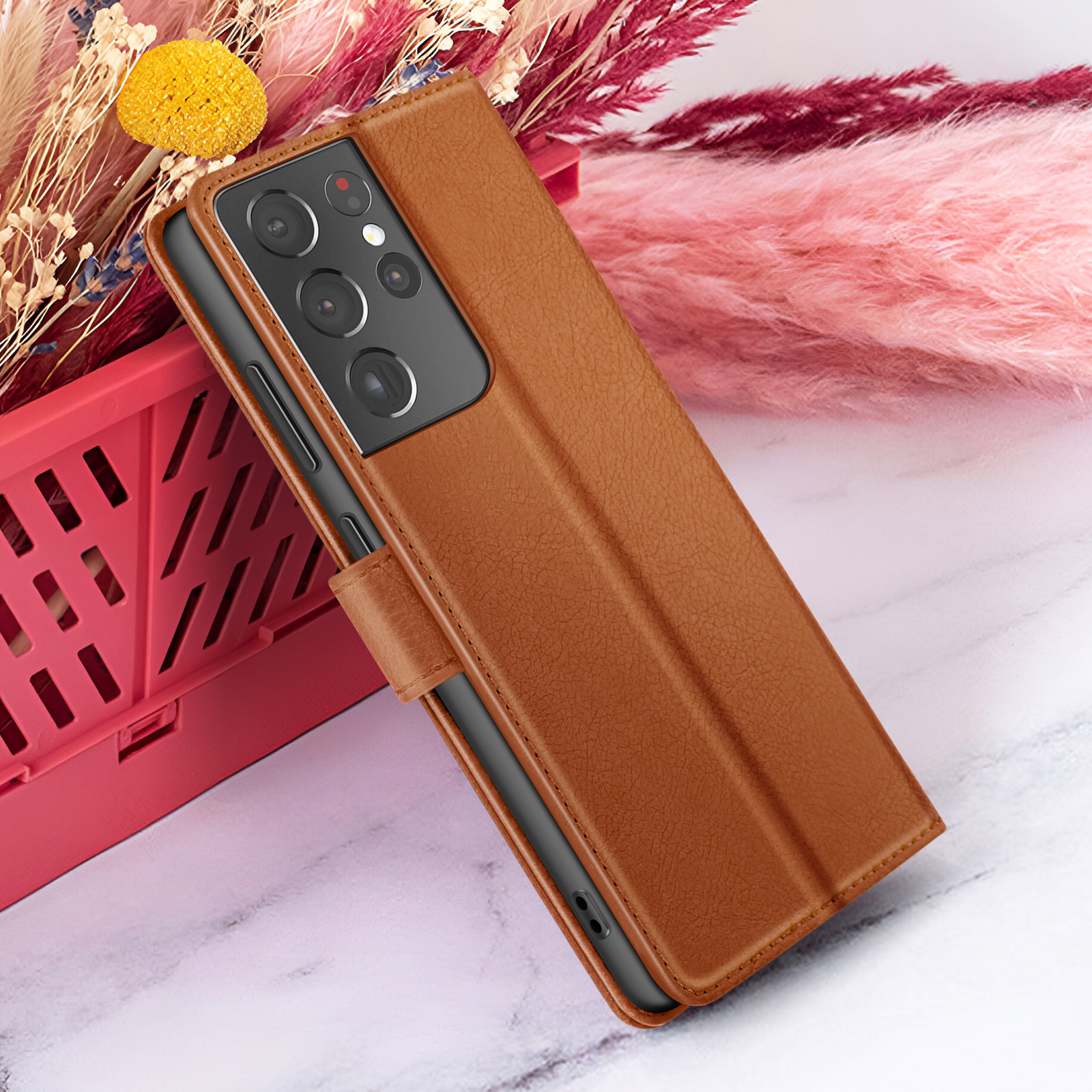 Un étui de téléphone en cuir marron avec un téléphone à l'intérieur, sur une surface en marbre, des fleurs en arrière-plan.