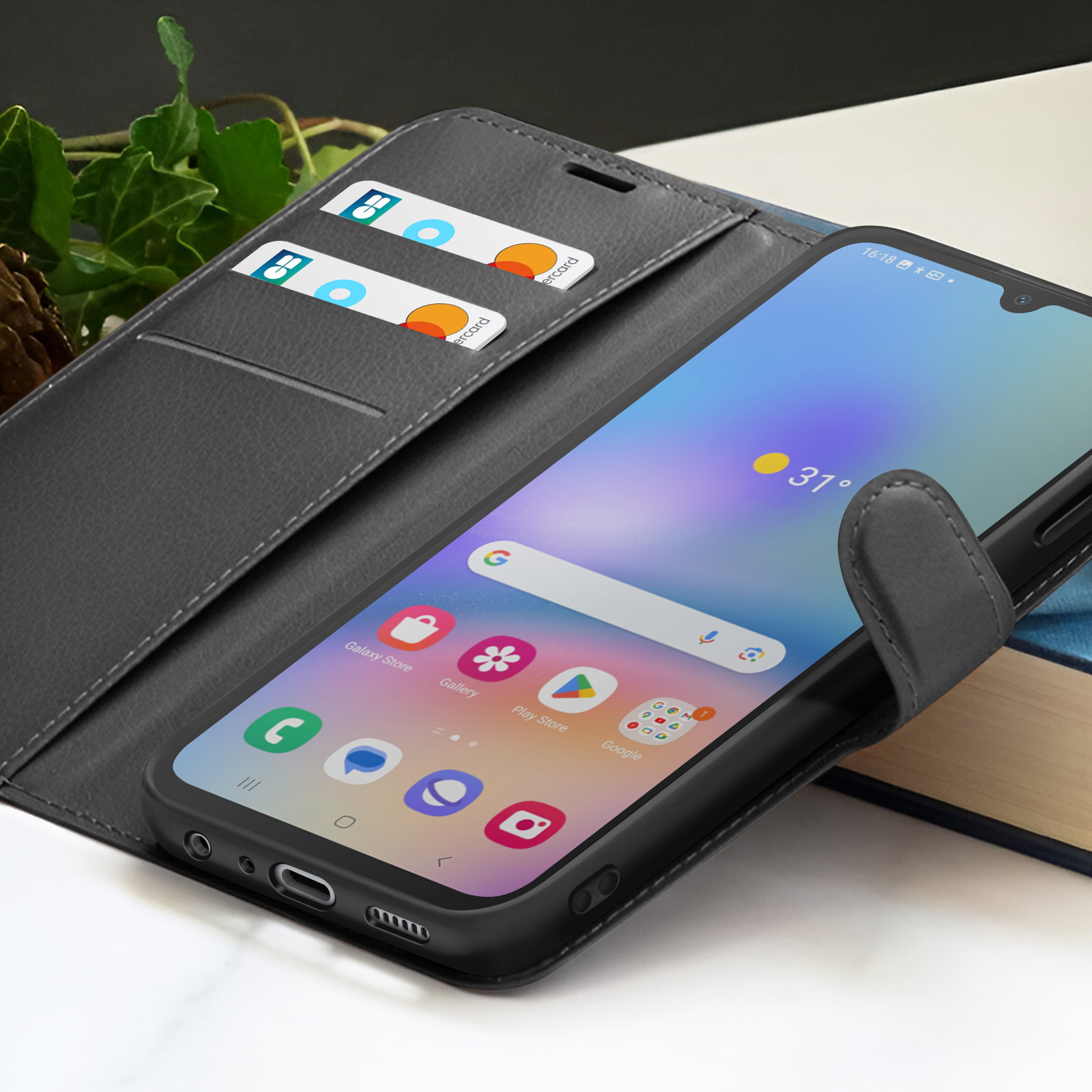 Een smartphone in een zwarte hoes toont apps en weer. Twee kaarten zitten in een sleuf. De hoes ligt op een boek.