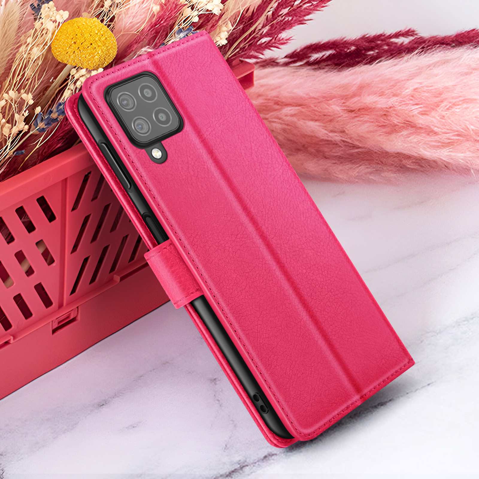 Een magenta telefoonhoesje is open en toont een zwarte telefoon. Gedroogde bloemen staan achter een rode krat.