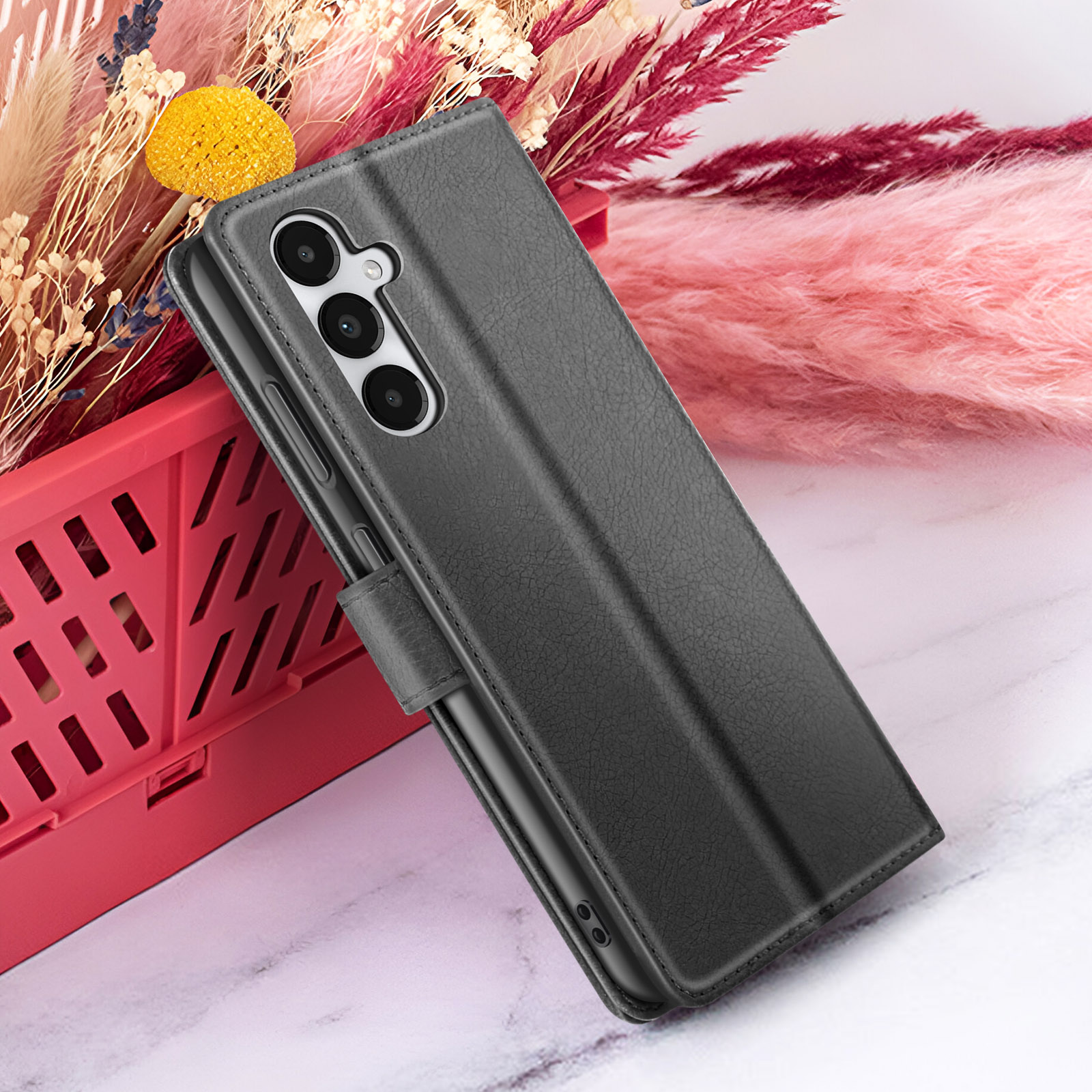 Een zwarte telefoonhoes met camera leunt tegen een rode container, met een roze en gele bloemenachtergrond.