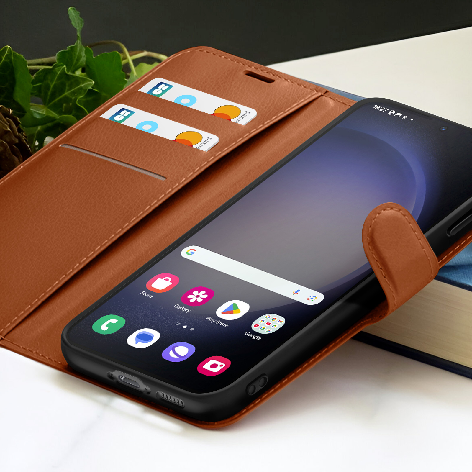 Een smartphone in een bruine leren hoes, met zichtbare creditcards. Het scherm toont app-iconen en een Google-zoekbalk.