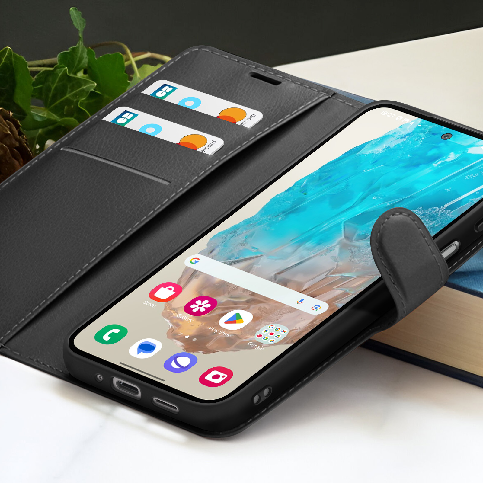Un smartphone dans un étui portefeuille noir avec cartes de crédit et un livre. L'écran affiche des applications et un fond bleu.