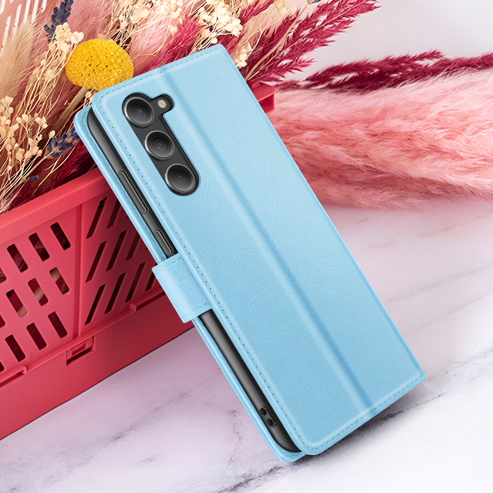 Un étui de téléphone bleu clair avec un téléphone à l'intérieur, à côté d'un conteneur rouge et de fleurs séchées.