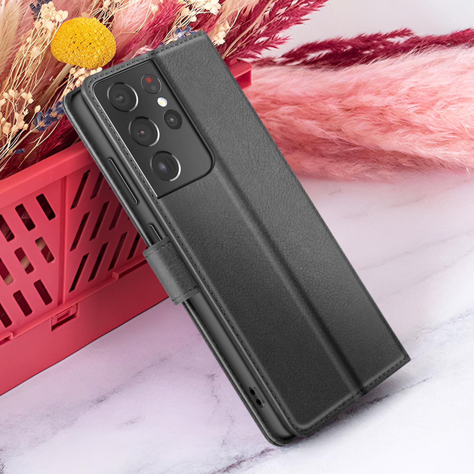 Een zwarte telefoonhoes met een telefoon erin, geplaatst naast roze bloemen en een rode container.
