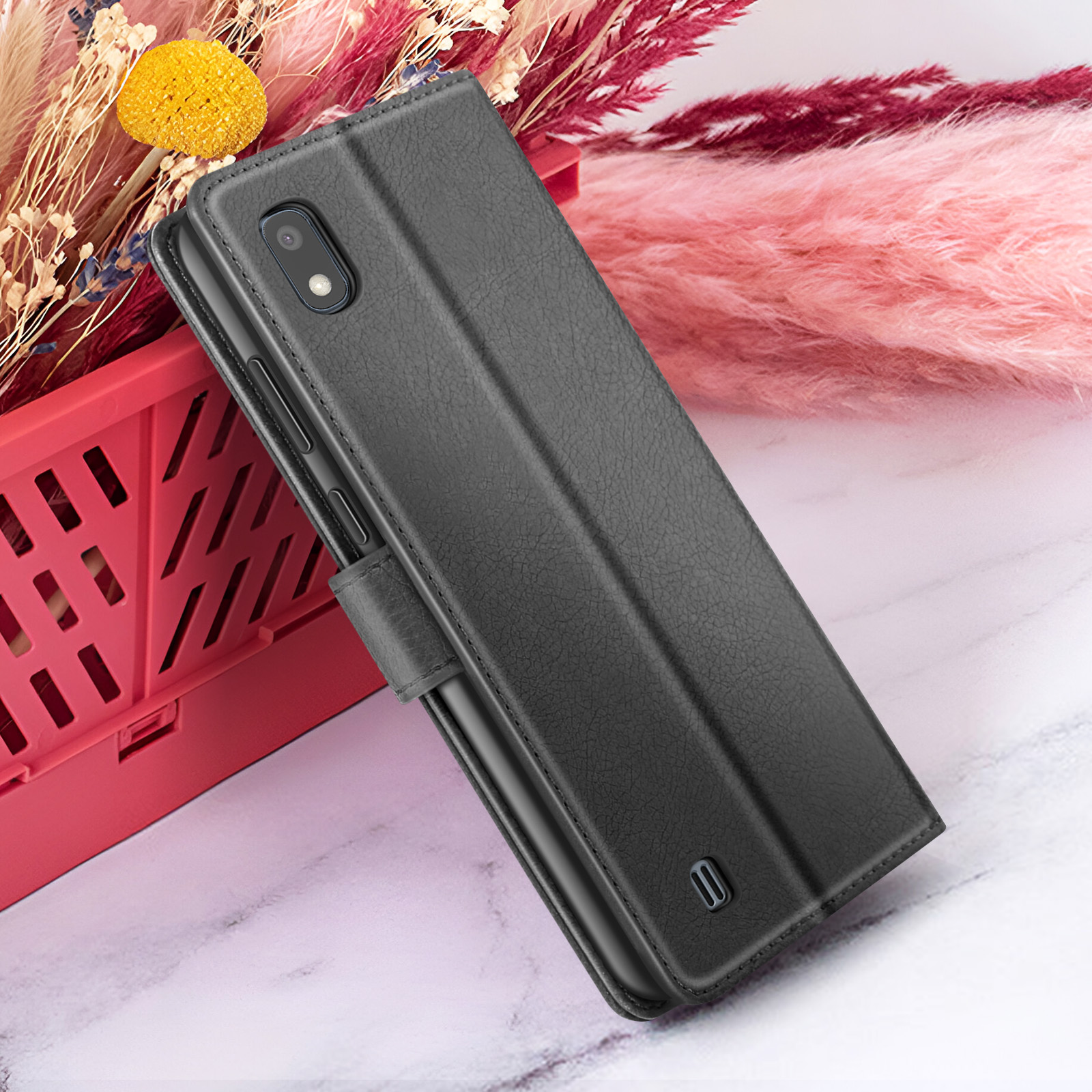 Custodia nera per telefono su superficie di marmo. Sfondo con elementi decorativi rosa e rossi e un cestino rosso.