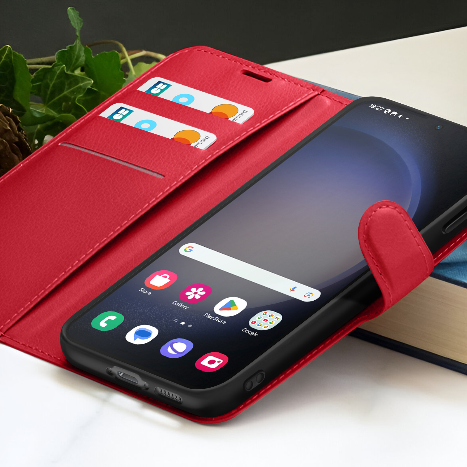 Un étui de téléphone rouge avec un smartphone. Des cartes de crédit sont visibles. Le téléphone affiche des icônes d'applications. Un livre en arrière-plan.