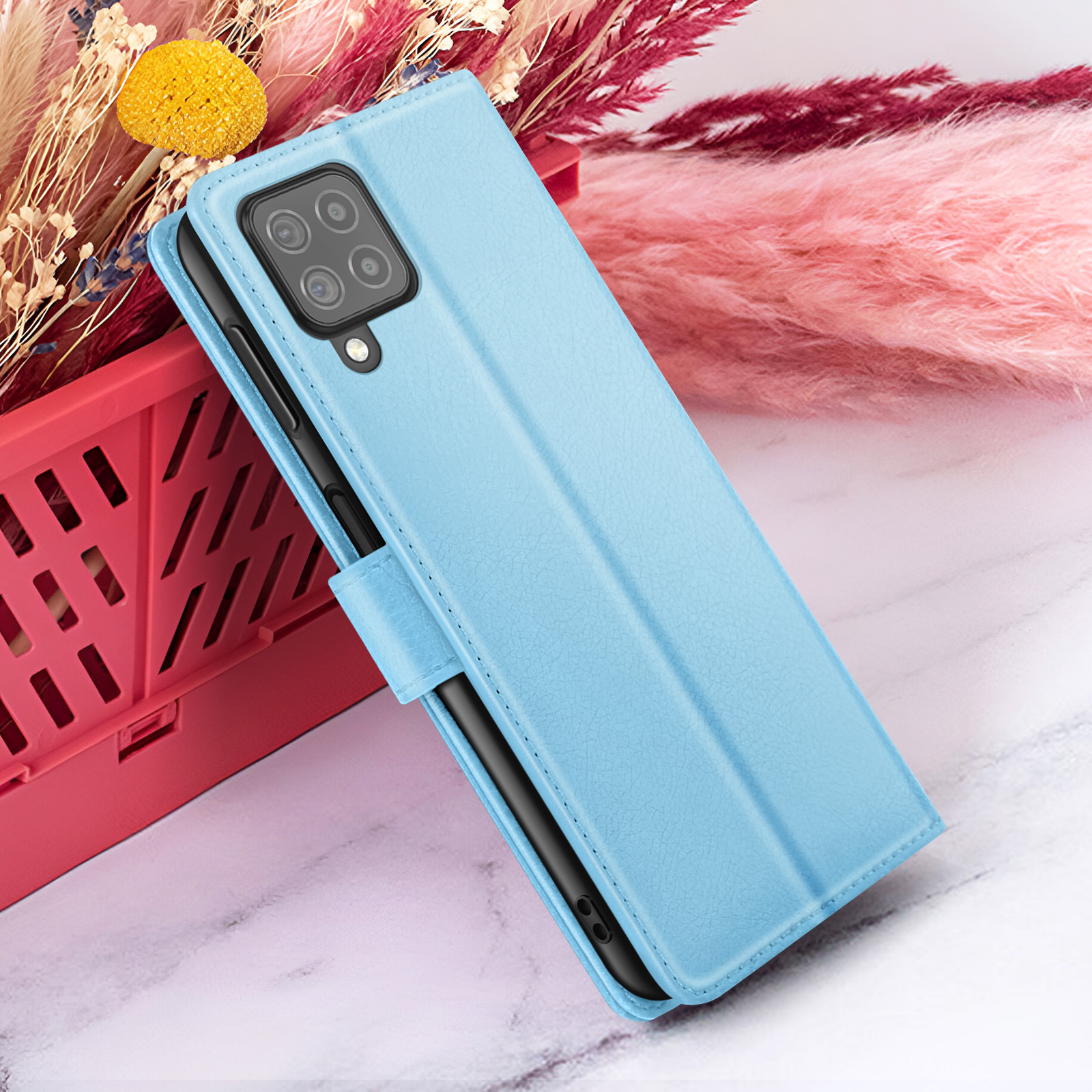 Een lichtblauwe telefoonhoes is open en onthult een zwarte telefoon. Het staat op een marmeren oppervlak met roze en rode decoraties.