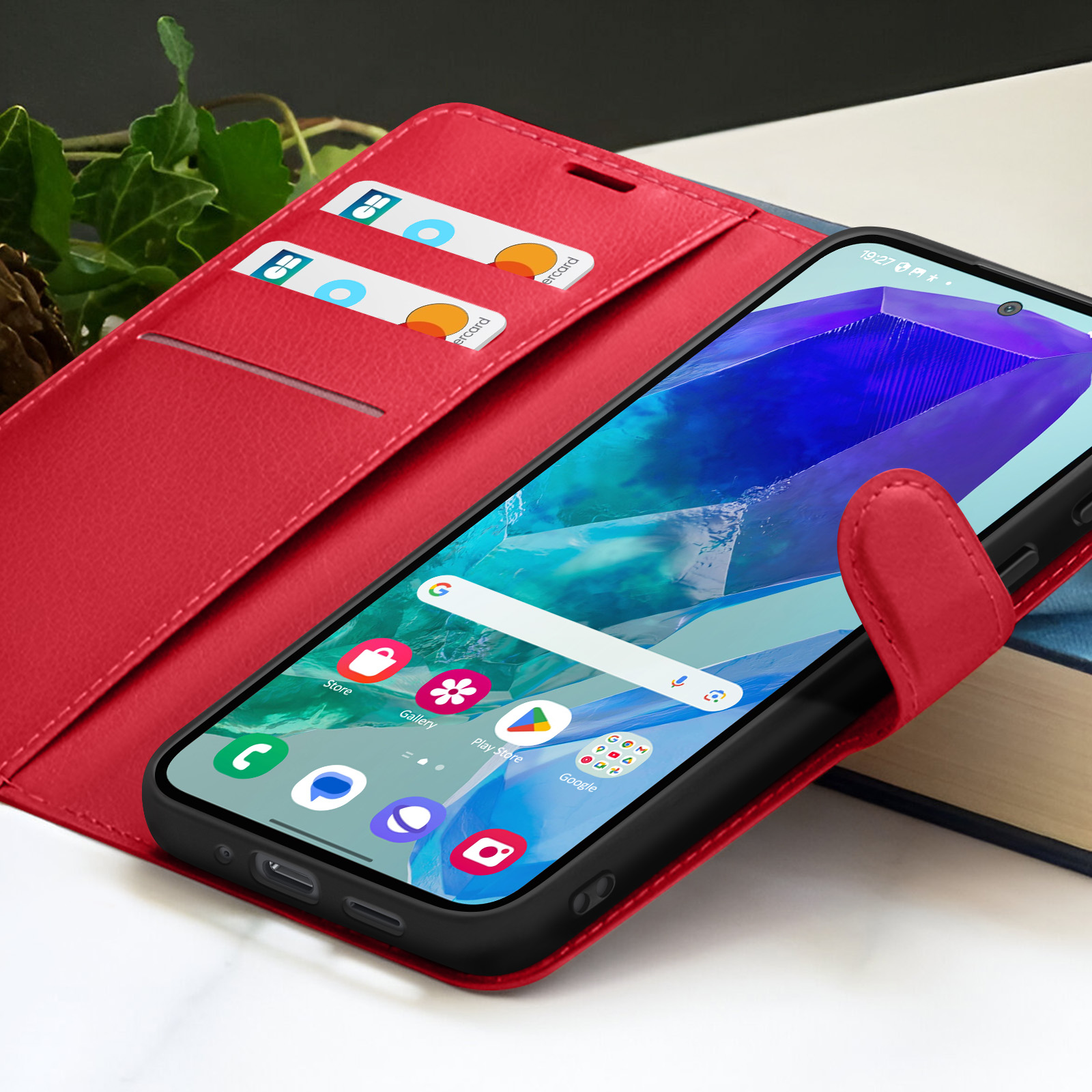 Custodia rossa per telefono con telefono all'interno, che mostra le icone delle app. Carte di credito nella custodia. Foglie verdi sullo sfondo.