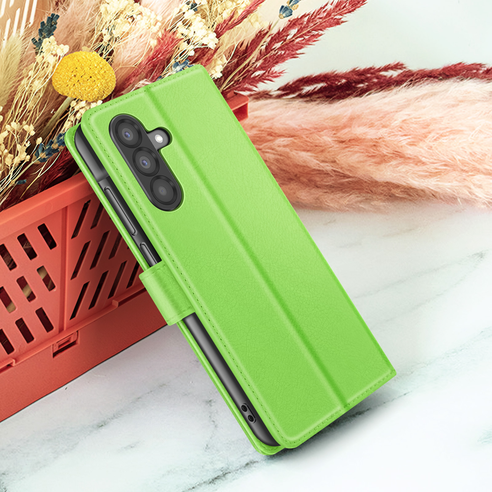 Een groene telefoonhoes met een telefoon erin, geplaatst op een wit oppervlak met bloemen op de achtergrond.