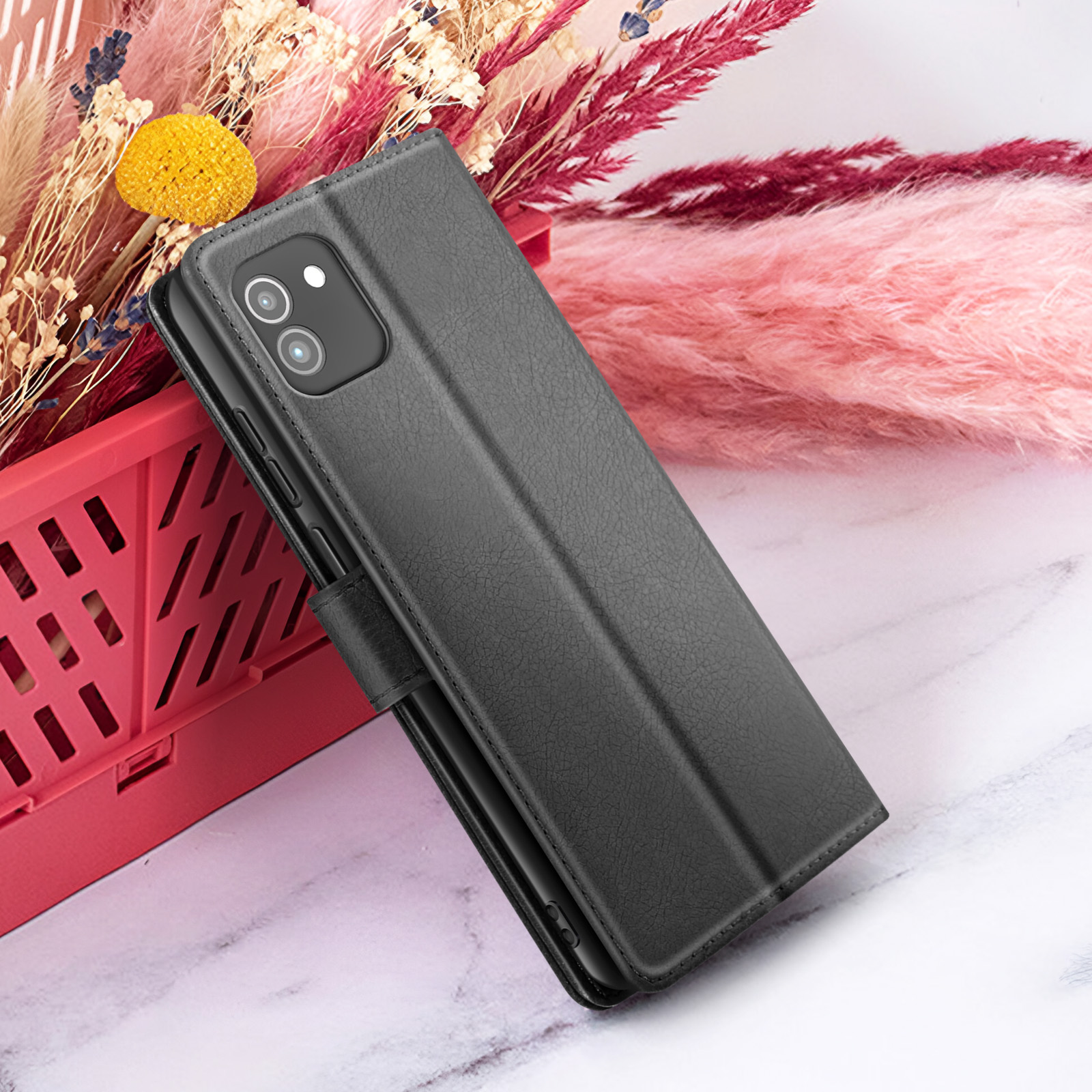 Zwarte telefoonhoes met camera, geplaatst op een marmeren oppervlak, met roze en rode bloemen op de achtergrond.