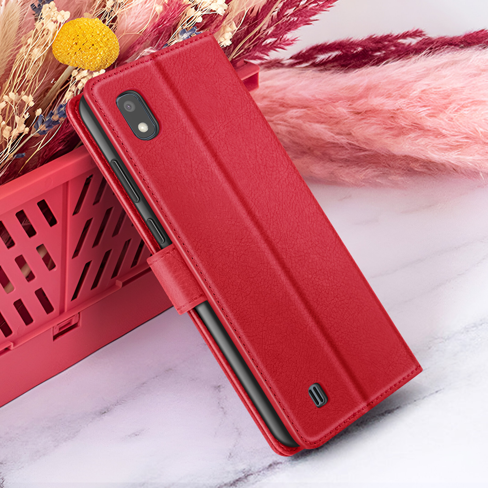 Una custodia rossa per telefono è aperta, accanto a un cestino rosso e fiori secchi. Sfondo marmoreo.