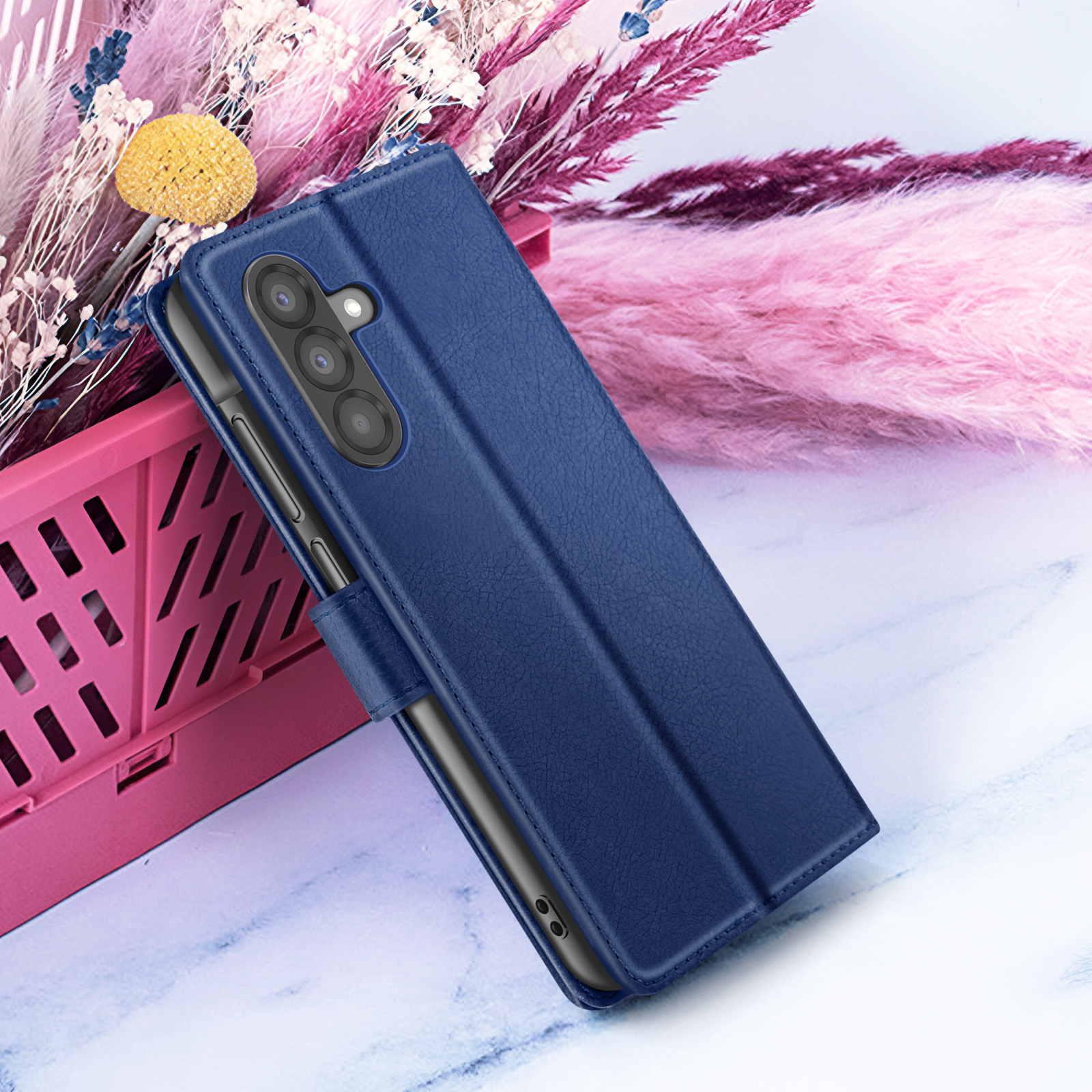 Un étui de téléphone bleu marine avec un téléphone à l'intérieur, placé devant des fleurs roses et violettes, sur une surface semblable au marbre.