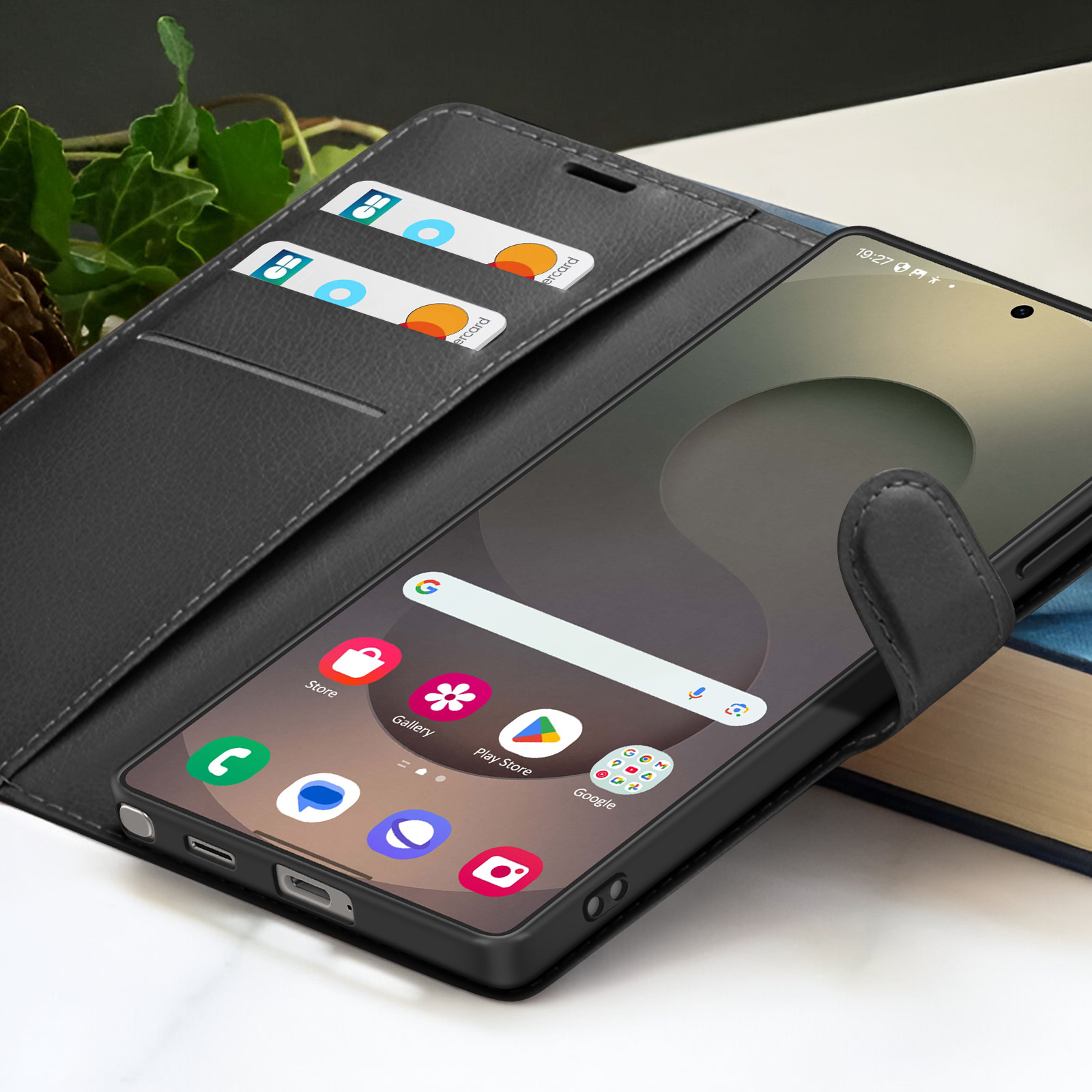Ein Smartphone in einer schwarzen Lederhülle mit sichtbaren Kreditkarten. Der Bildschirm zeigt Apps an, die Uhrzeit ist 19:27.