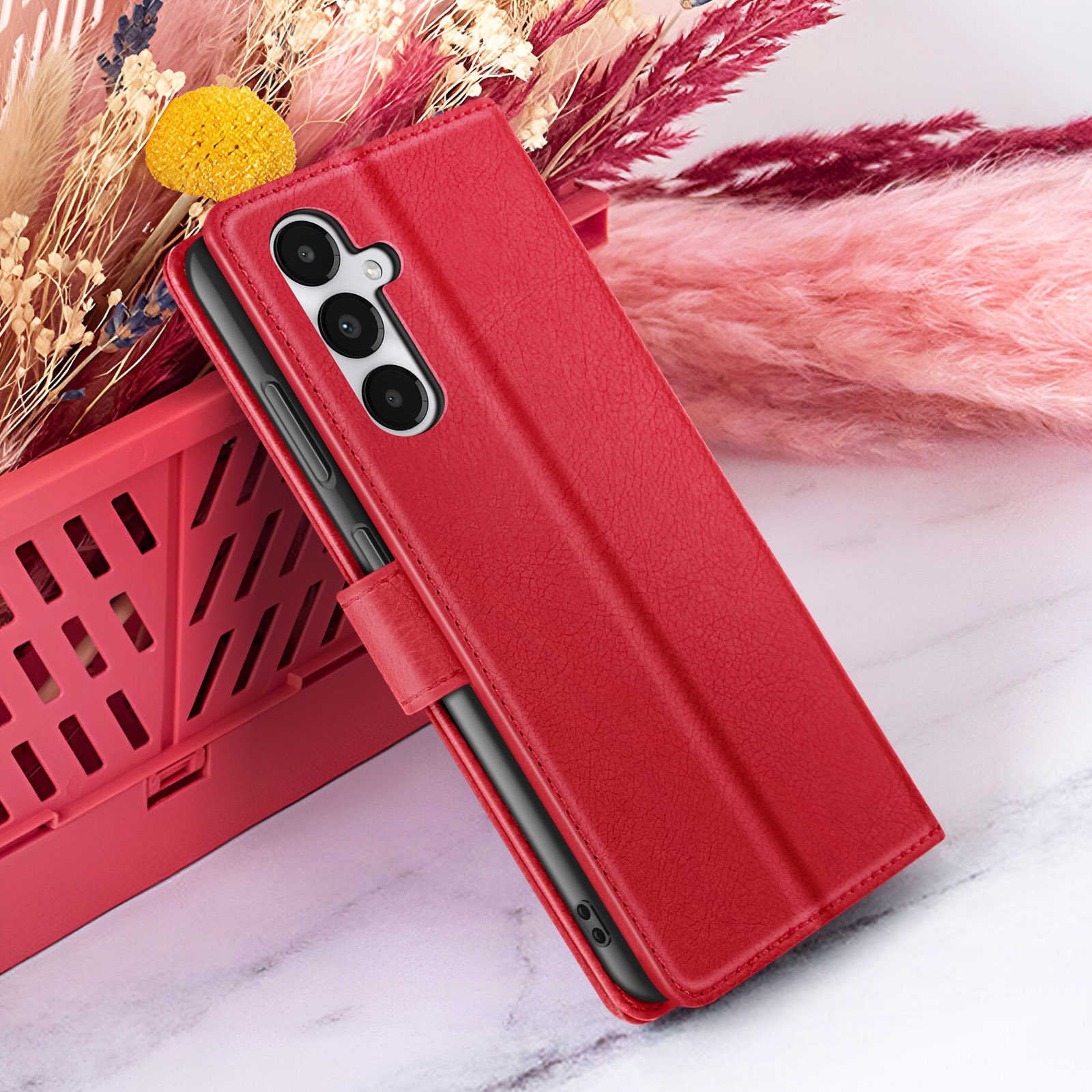 Un étui de téléphone rouge avec trois objectifs d'appareil photo est appuyé contre un panier rouge. Fond floral.