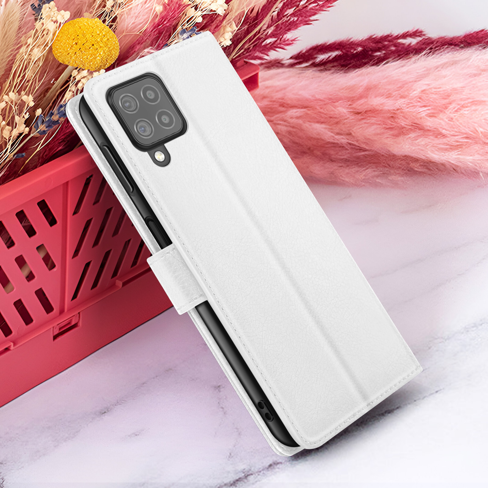Étui de téléphone blanc avec un téléphone noir à l'intérieur, posé devant des décorations roses et rouges, et sur une surface en marbre.