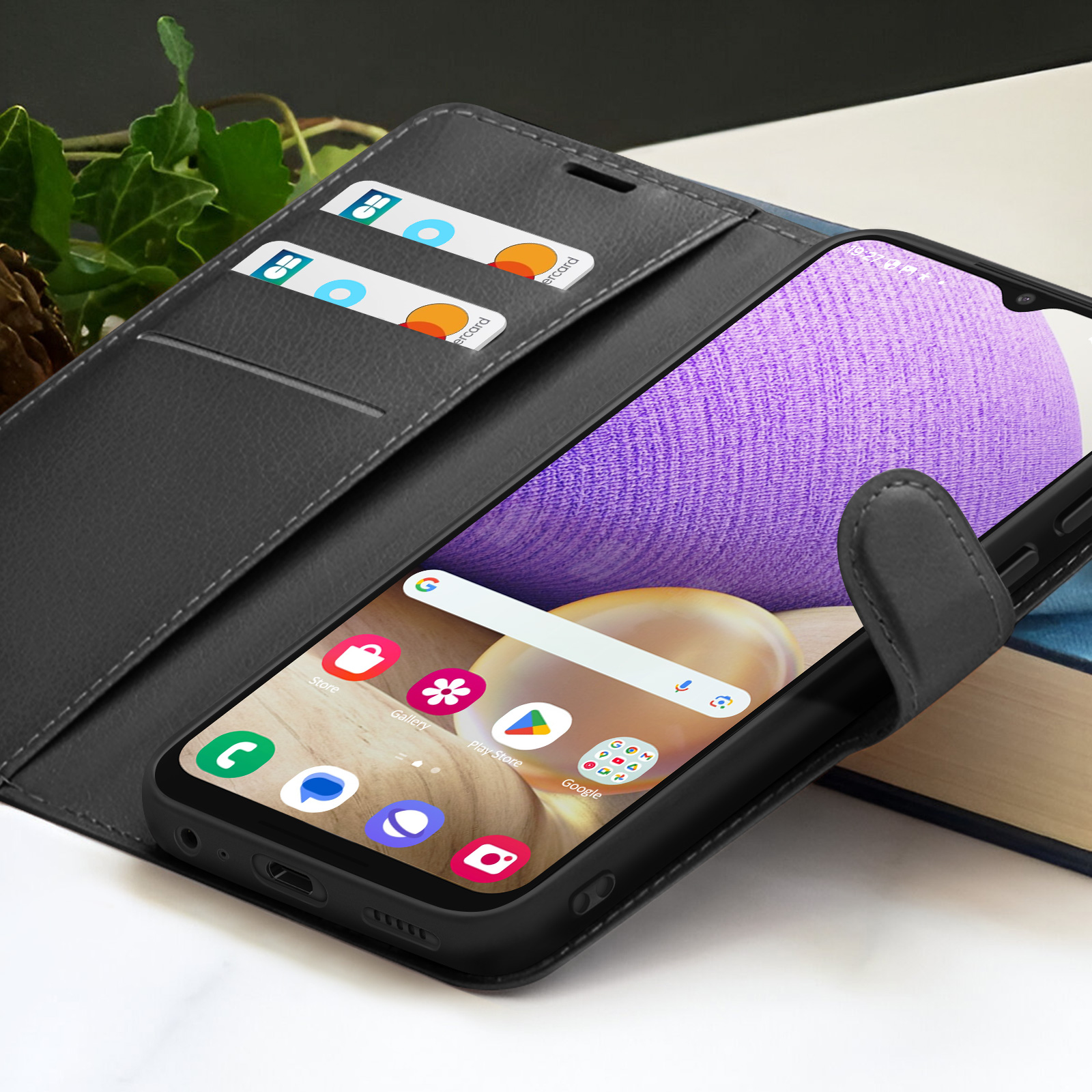 Ein Smartphone in einer schwarzen Hülle mit Startbildschirm. Kreditkarten in den Kartenfächern des Gehäuses. Bücher dahinter.