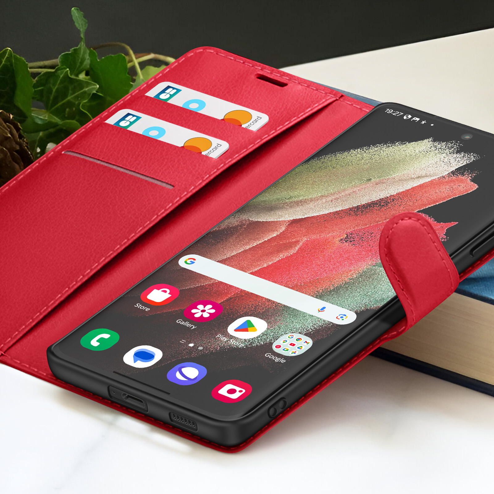 Een smartphone zit in een rode leren hoes. Creditcards zijn zichtbaar in een zak. Het scherm toont apps en tijd.