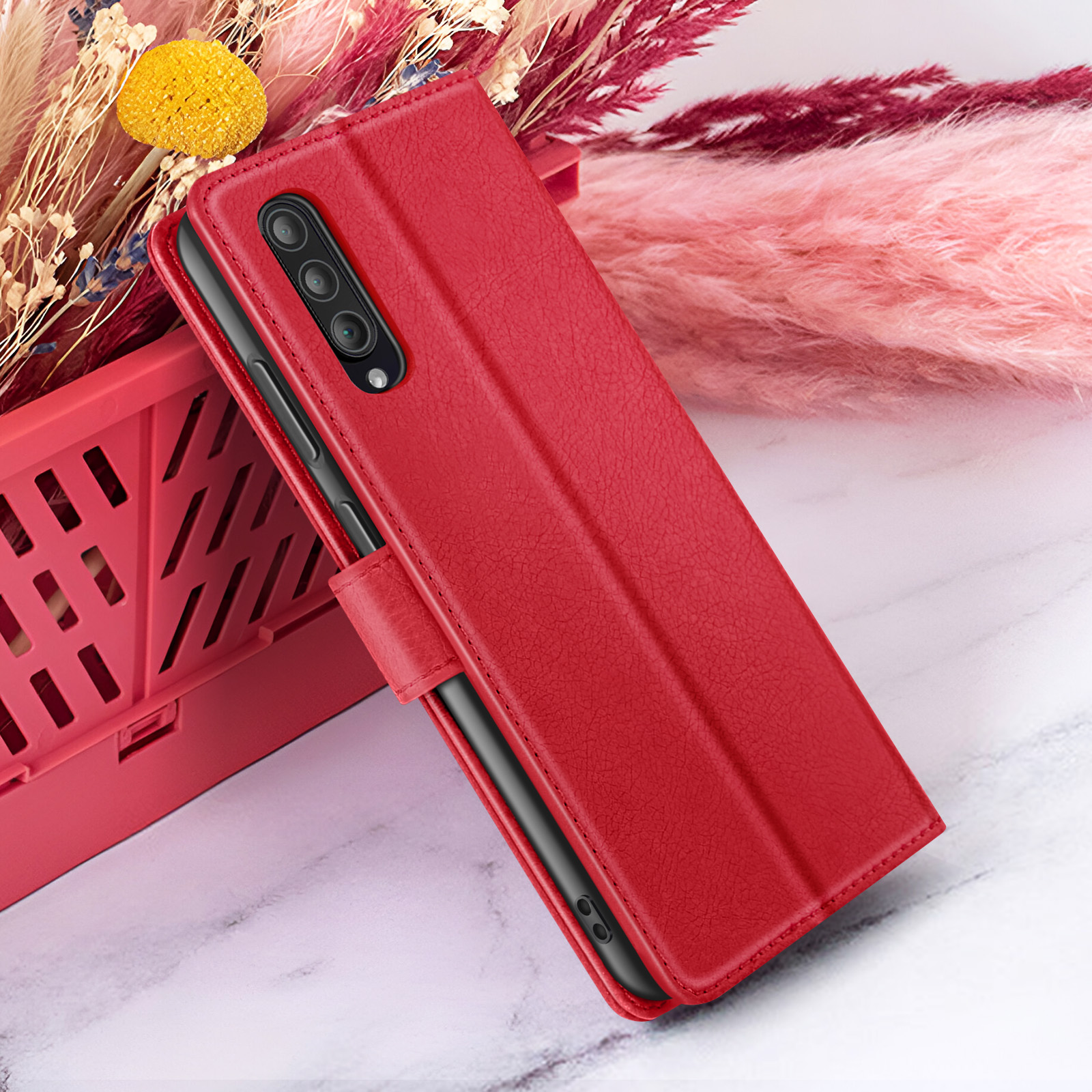 Custodia rossa per telefono su superficie di marmo, con fiori secchi sullo sfondo e un cestino rosso.