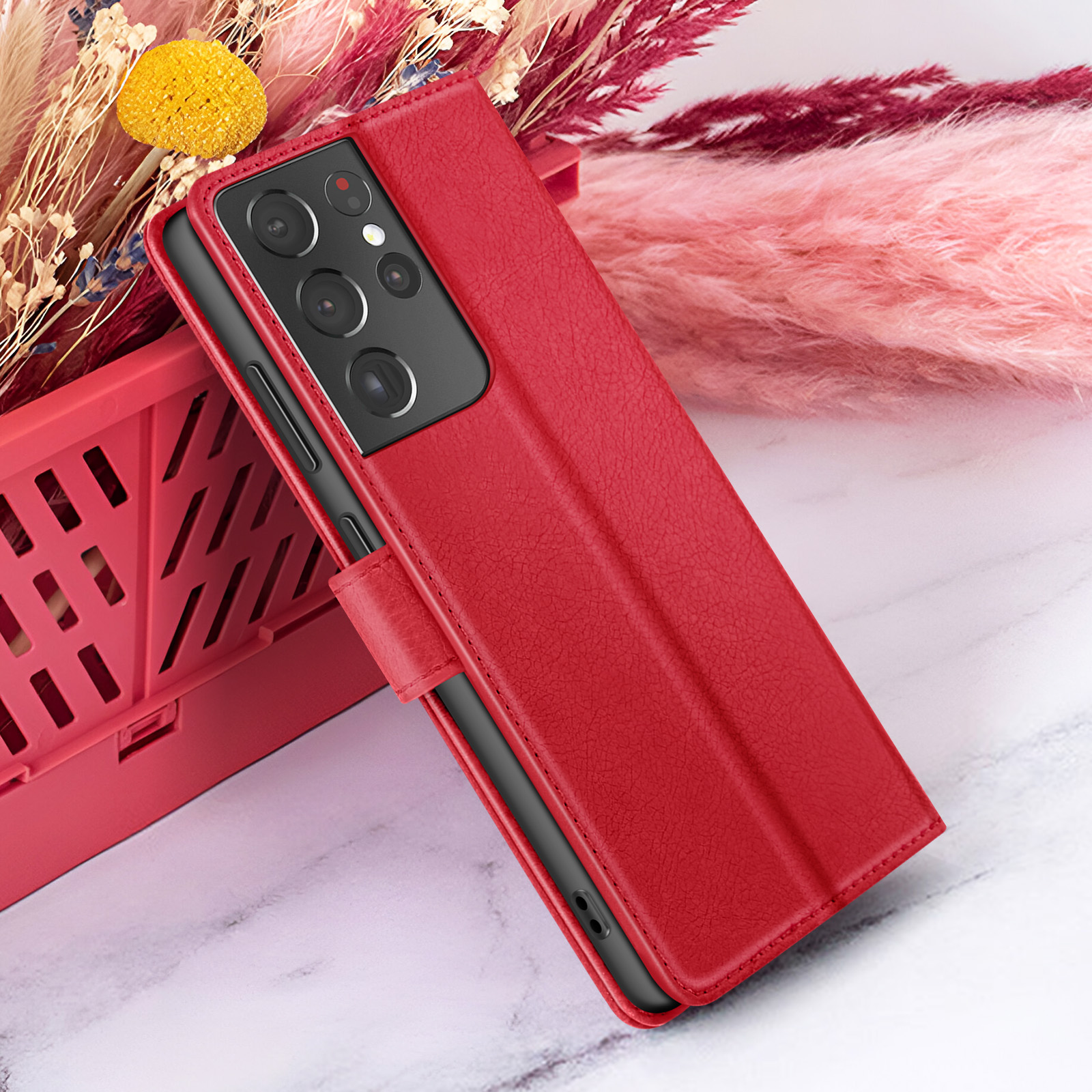 Rode telefoonhoes met telefoon, rustend op een marmeren oppervlak met roze en rode bloemen op de achtergrond.