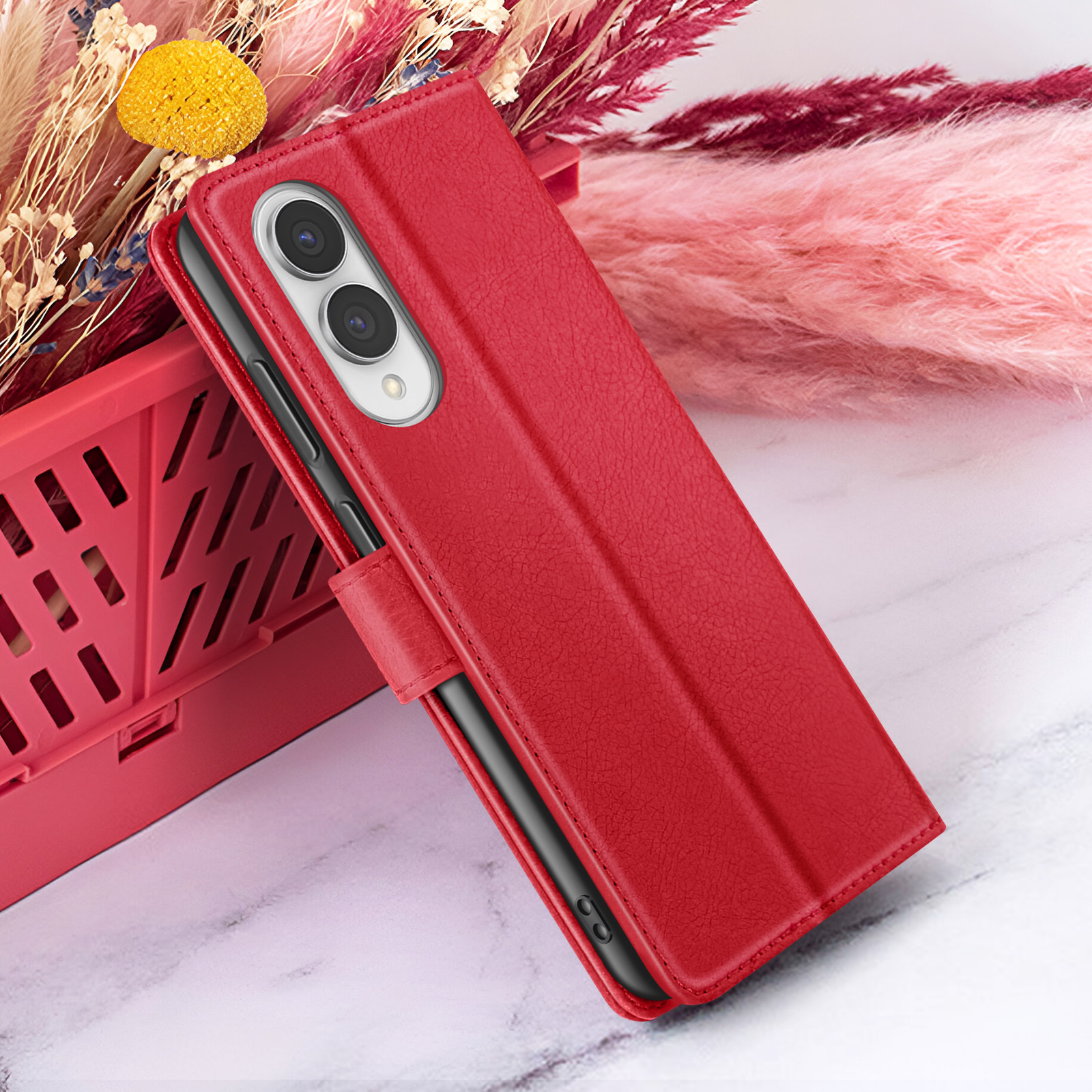 Étui de téléphone rouge avec téléphone à l'intérieur. Fleurs et panier rouge en arrière-plan sur marbre.