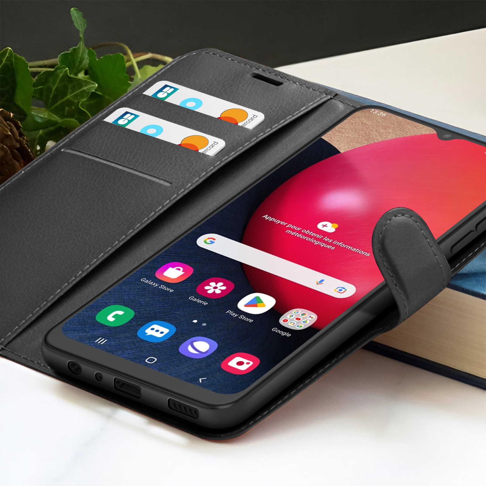Een zwarte smartphone in een grijze hoes toont het startscherm. Creditcards zijn zichtbaar in de sleuven van de hoes. Achtergrond toont een boek.
