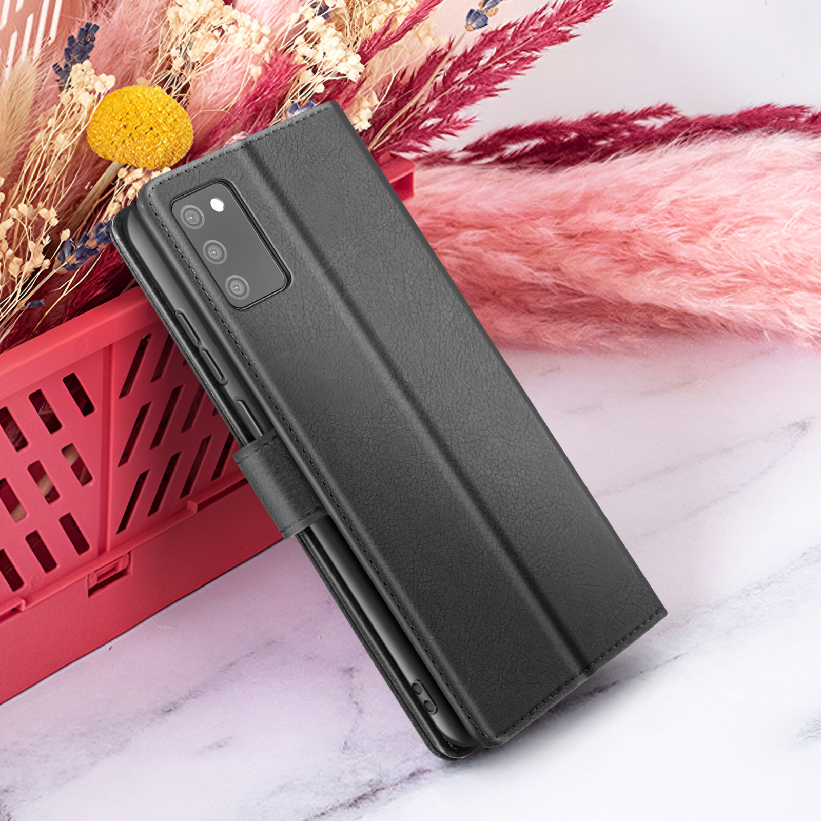 Een zwarte telefoonhoes rust tegen roze en rode bloemen. Een rode mand staat op de achtergrond. De achtergrond is marmer.