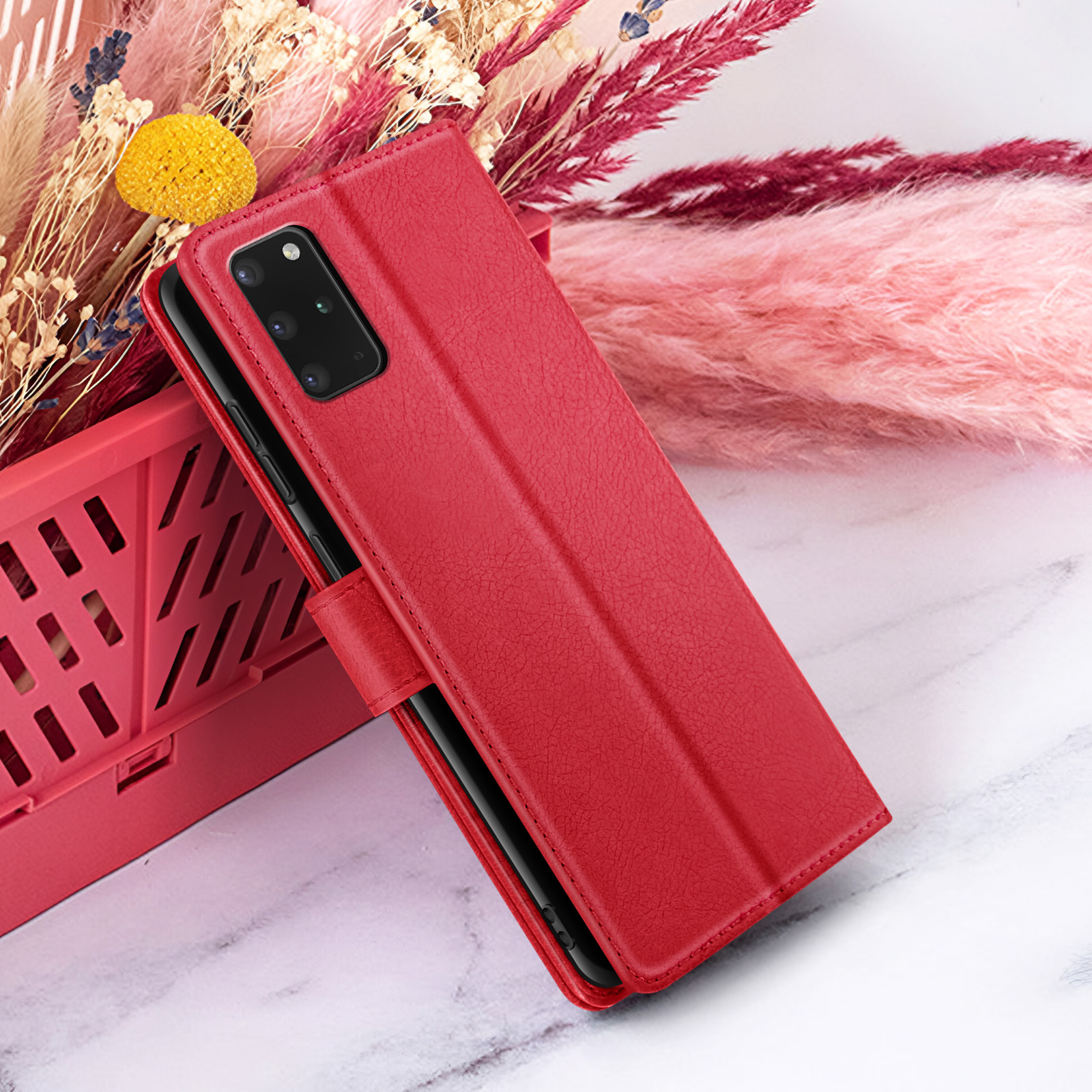 Rode telefoonhoes op wit marmer. Achter, roze en bordeauxrode gedroogde bloemen en een rode mand.