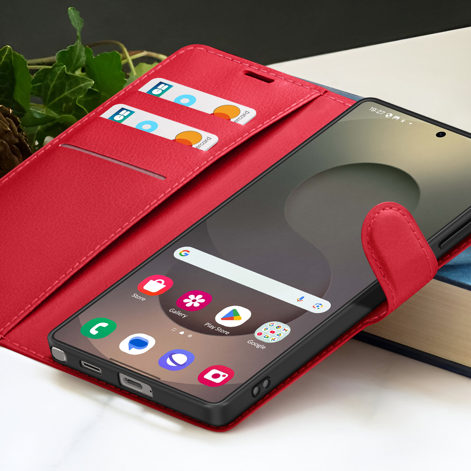 Ein Smartphone in einer roten Hülle zeigt Apps an. Kreditkarten sind in der Hülle sichtbar. Bücher sind im Hintergrund.