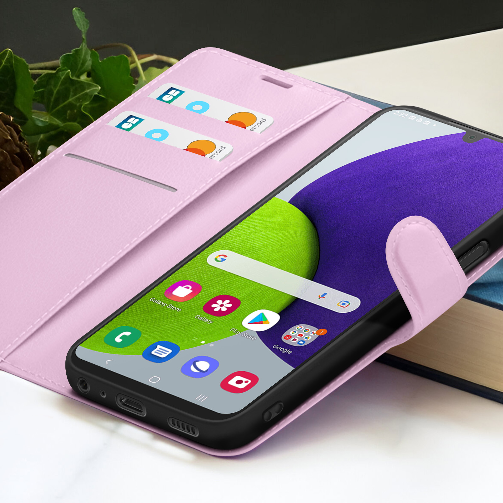 Roze telefoonhoesje met telefoon erin. Het scherm toont app-iconen. Kaarten zichtbaar in de hoes. Groene en paarse achtergrond.