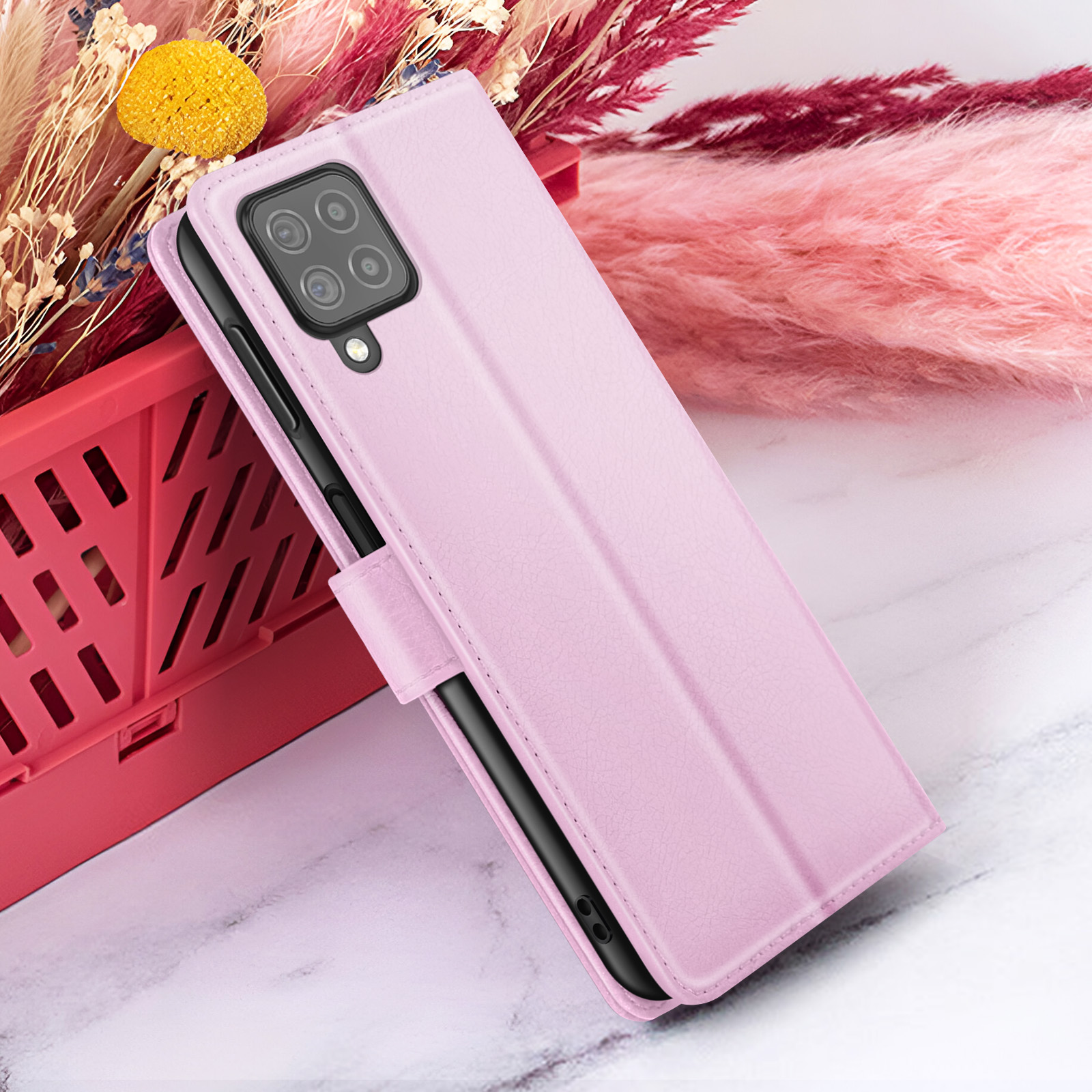Een roze telefoonhoesje met een telefoon erin, geplaatst naast roze en rode decoratieve planten, op een marmeren oppervlak.