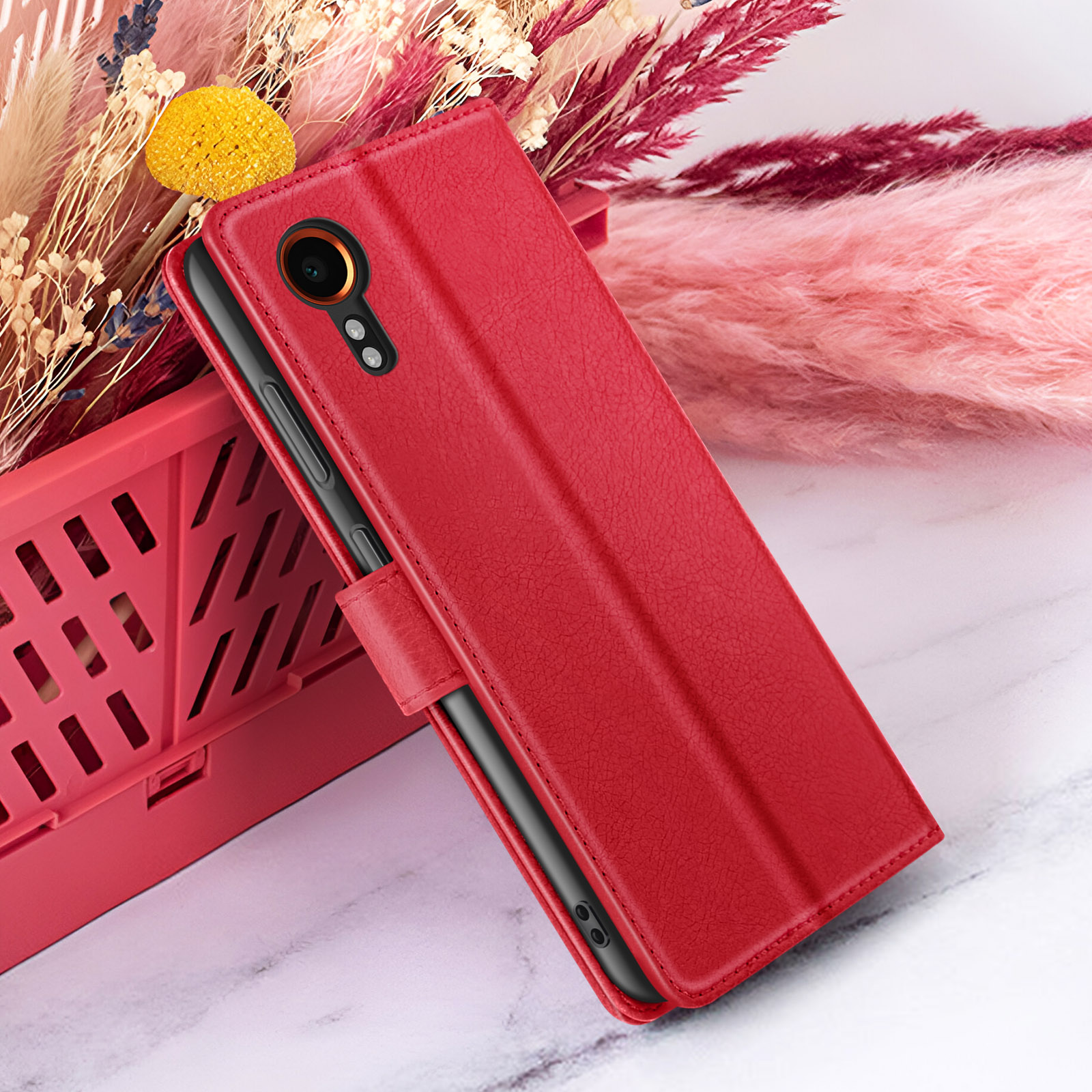 Étui de téléphone rouge avec un téléphone à l'intérieur. Le fond présente des fleurs roses et beiges. L'étui est sur un plateau rouge.