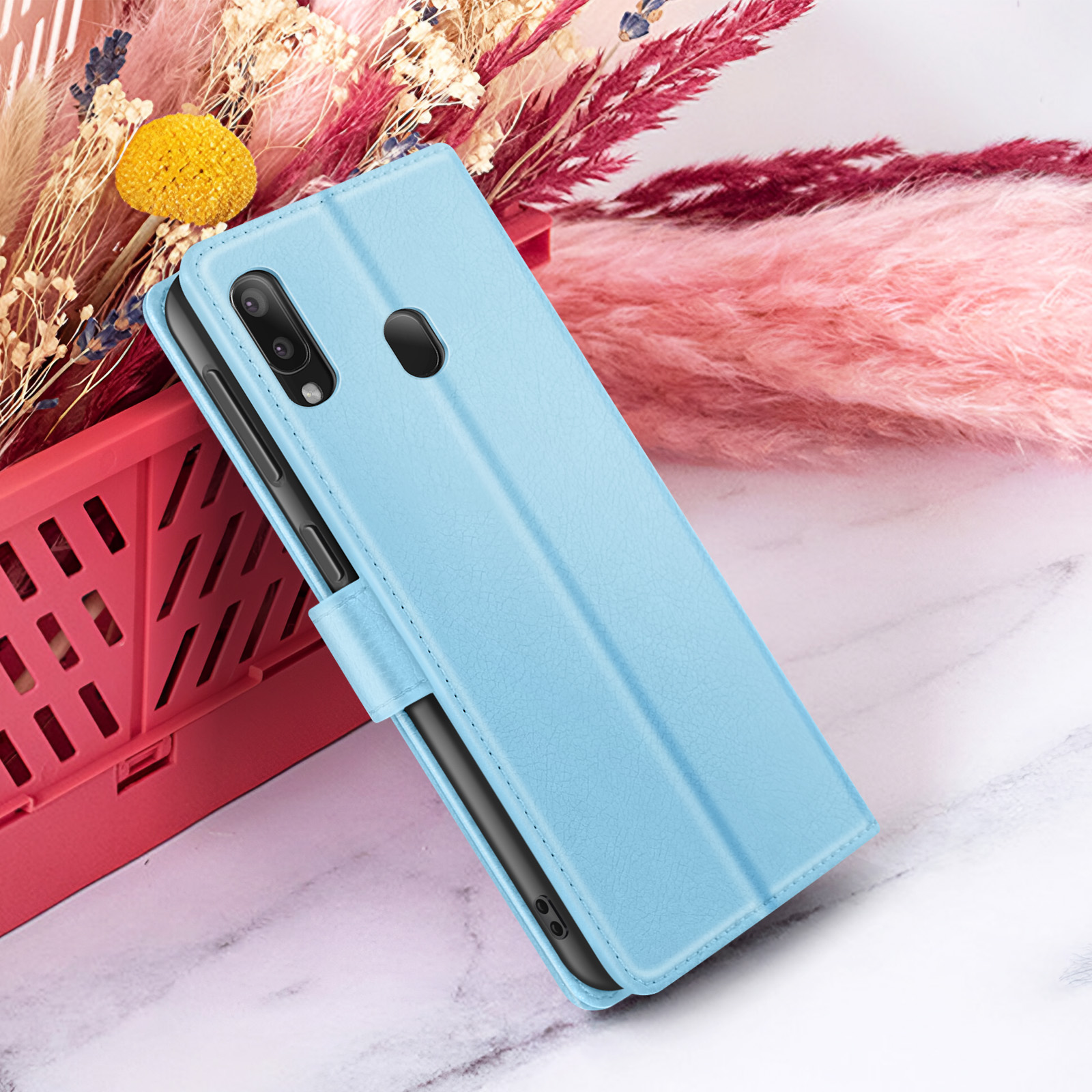 Een blauwe telefoonhoes is open en onthult een telefoon. Bloemenachtergrond met roze en beige tinten. Rode plastic mand.