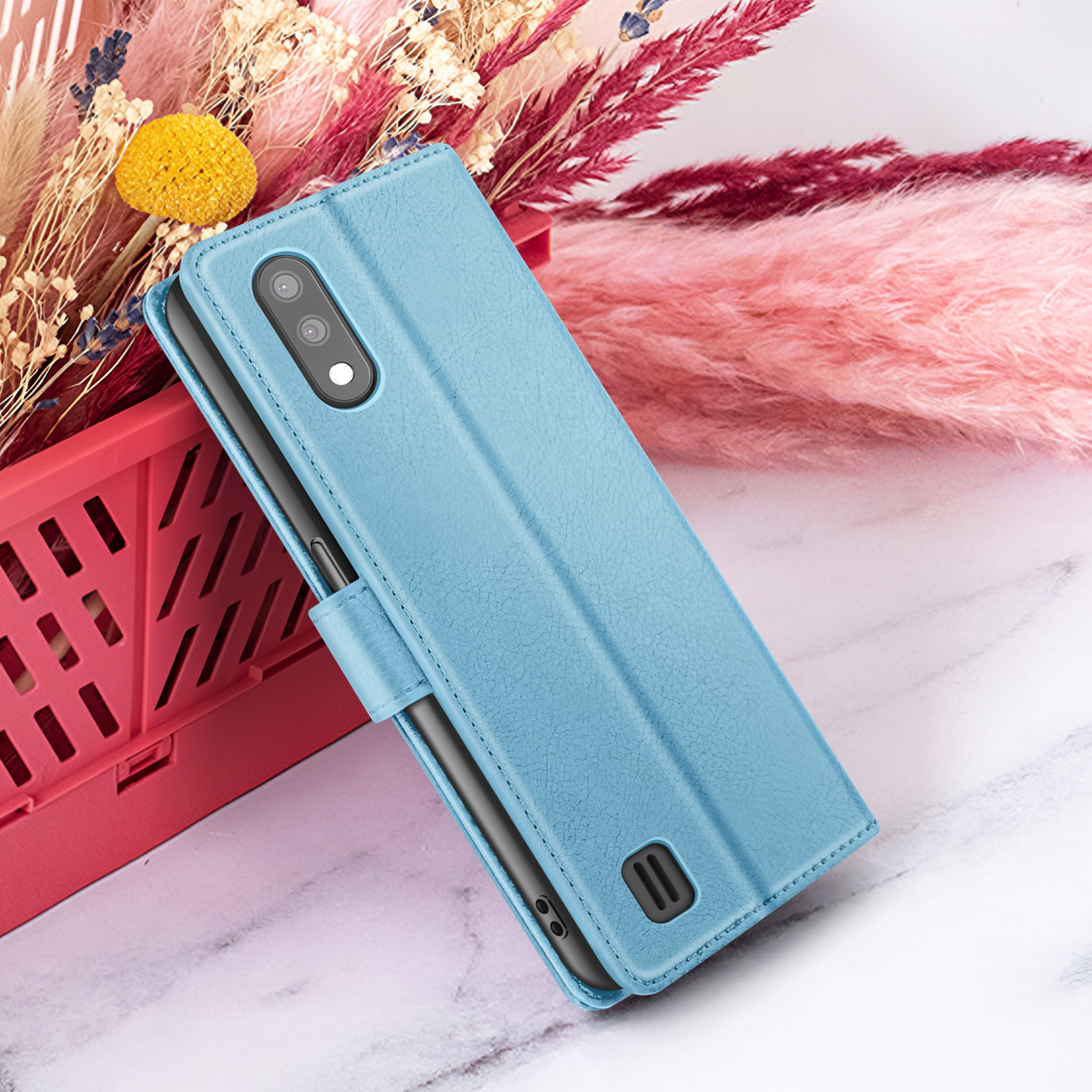 Een lichtblauwe telefoonhoes met een telefoon erin, voor gedroogde bloemen en een roze achtergrond.