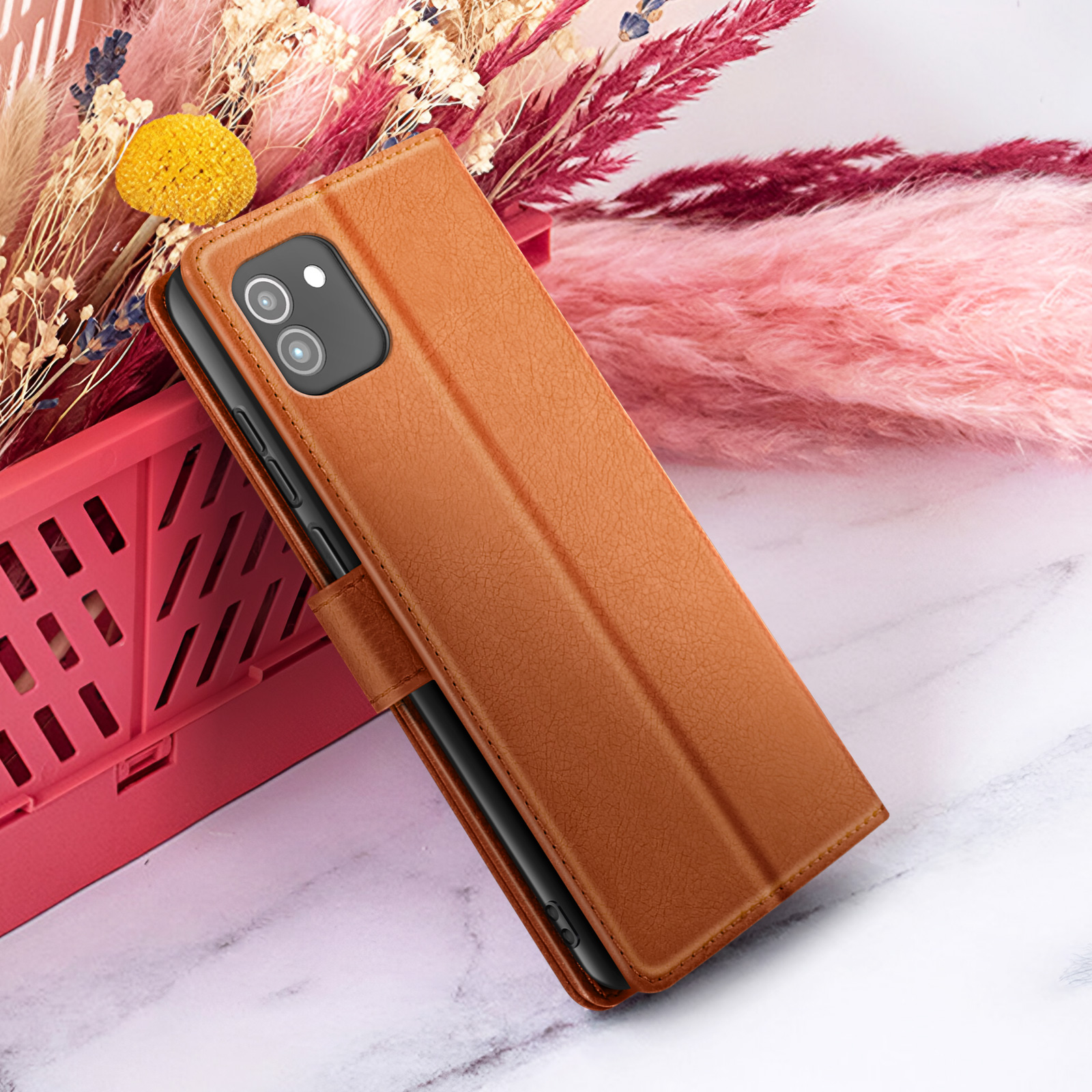 Un étui de téléphone marron est ouvert, reposant contre un fond avec des fleurs et une surface semblable au marbre.