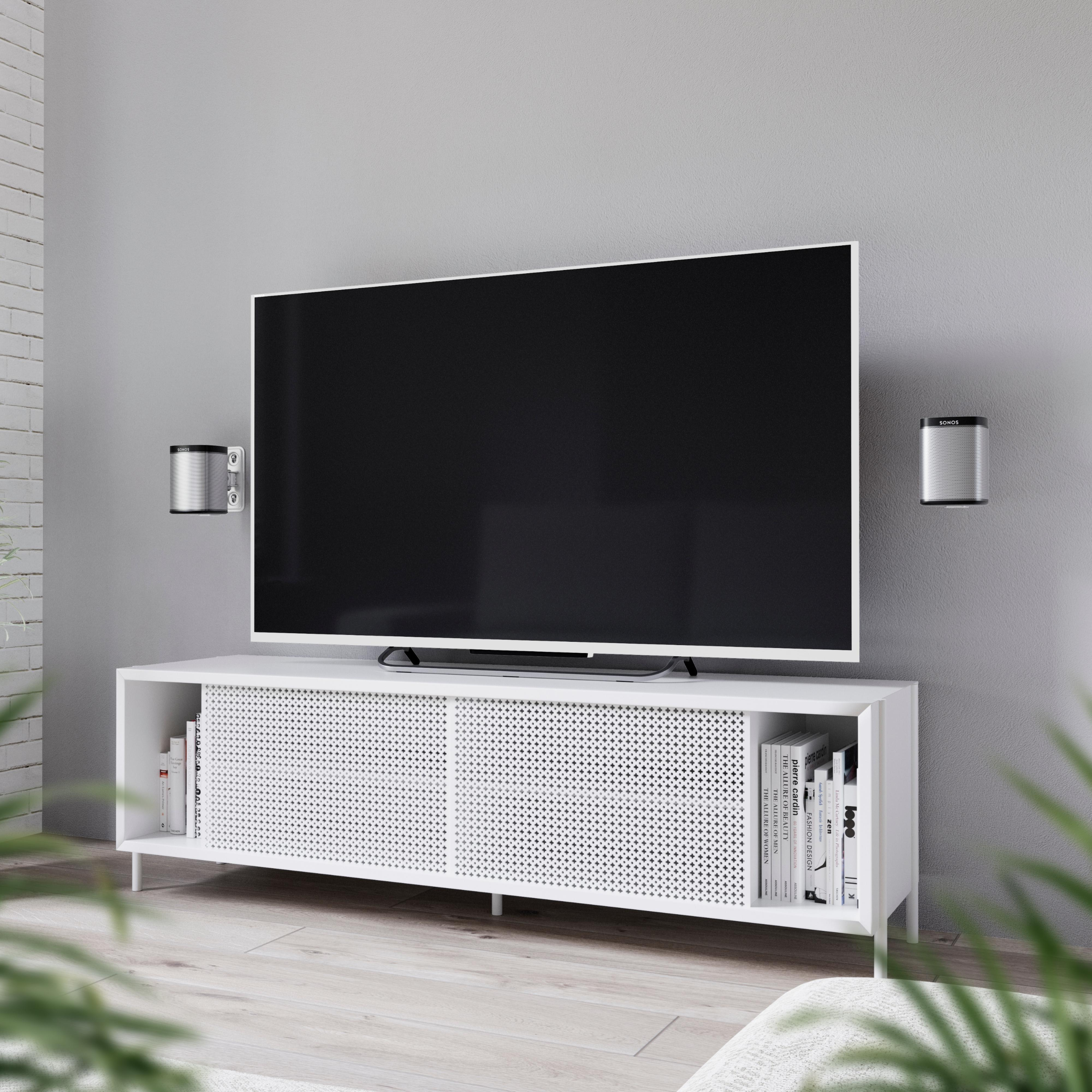 Ein Fernseher auf einem weißen Schrank. Zwei Lautsprecher sind an der grauen Wand montiert. Bücher und Pflanzen sind zu sehen.