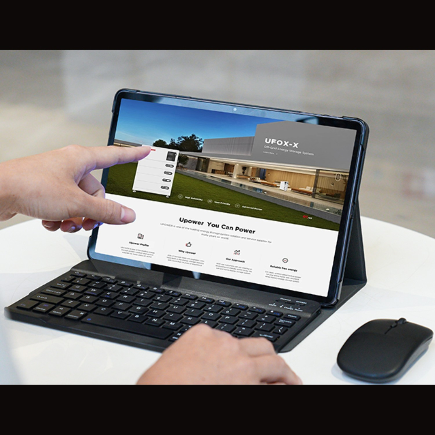 Dłoń dotyka ekranu tabletu z 'UFOX-X'. Klawiatura i mysz na białym stole.